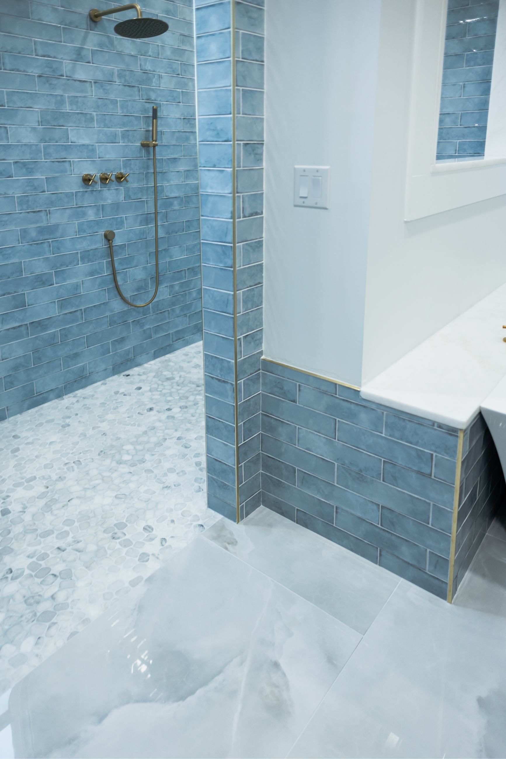 Blue-tiled walk-in shower with handheld showerhead and a bench seat in a white bathroom.