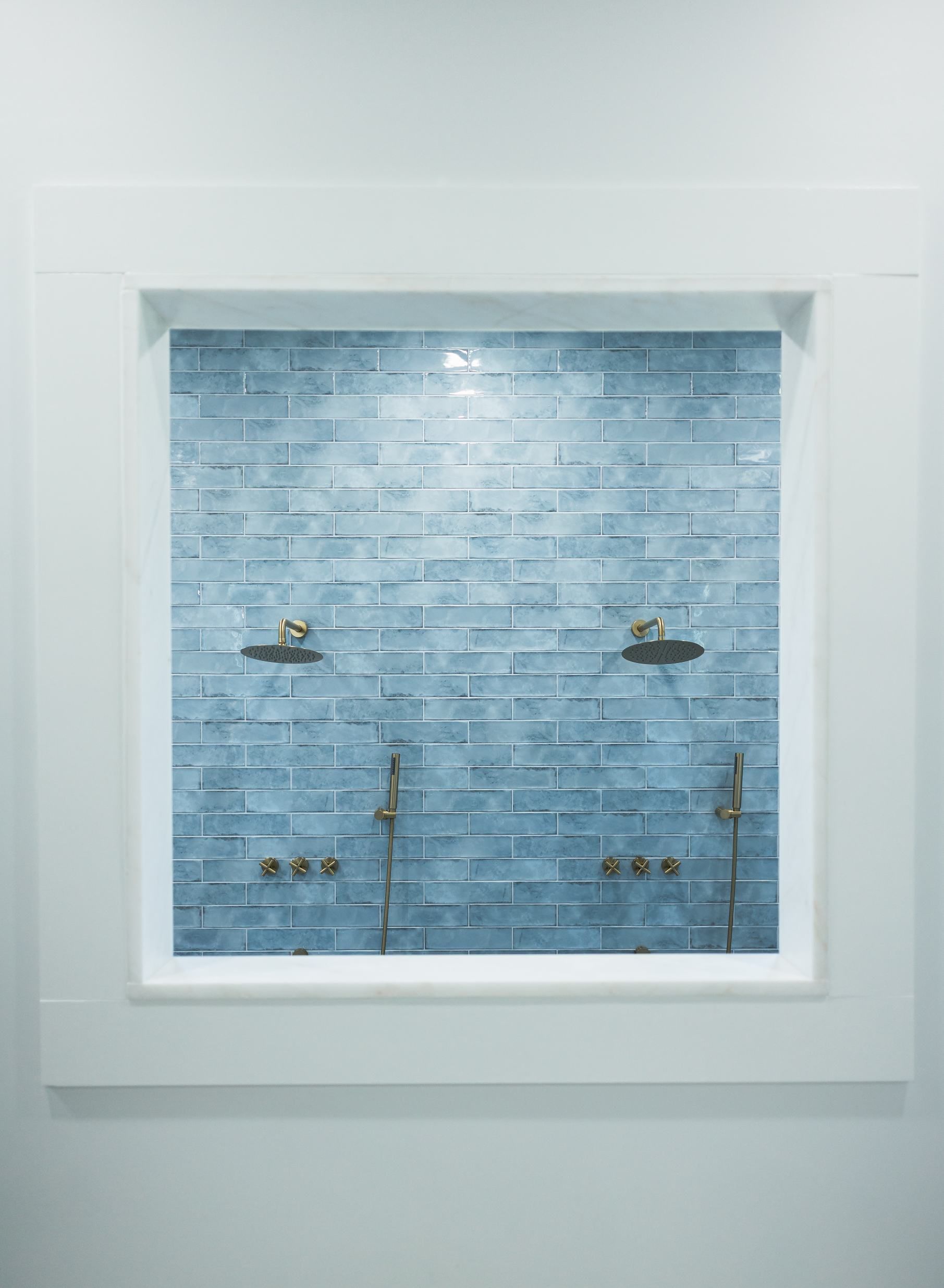 White-framed shower niche with blue subway tile and chrome fixtures inside.