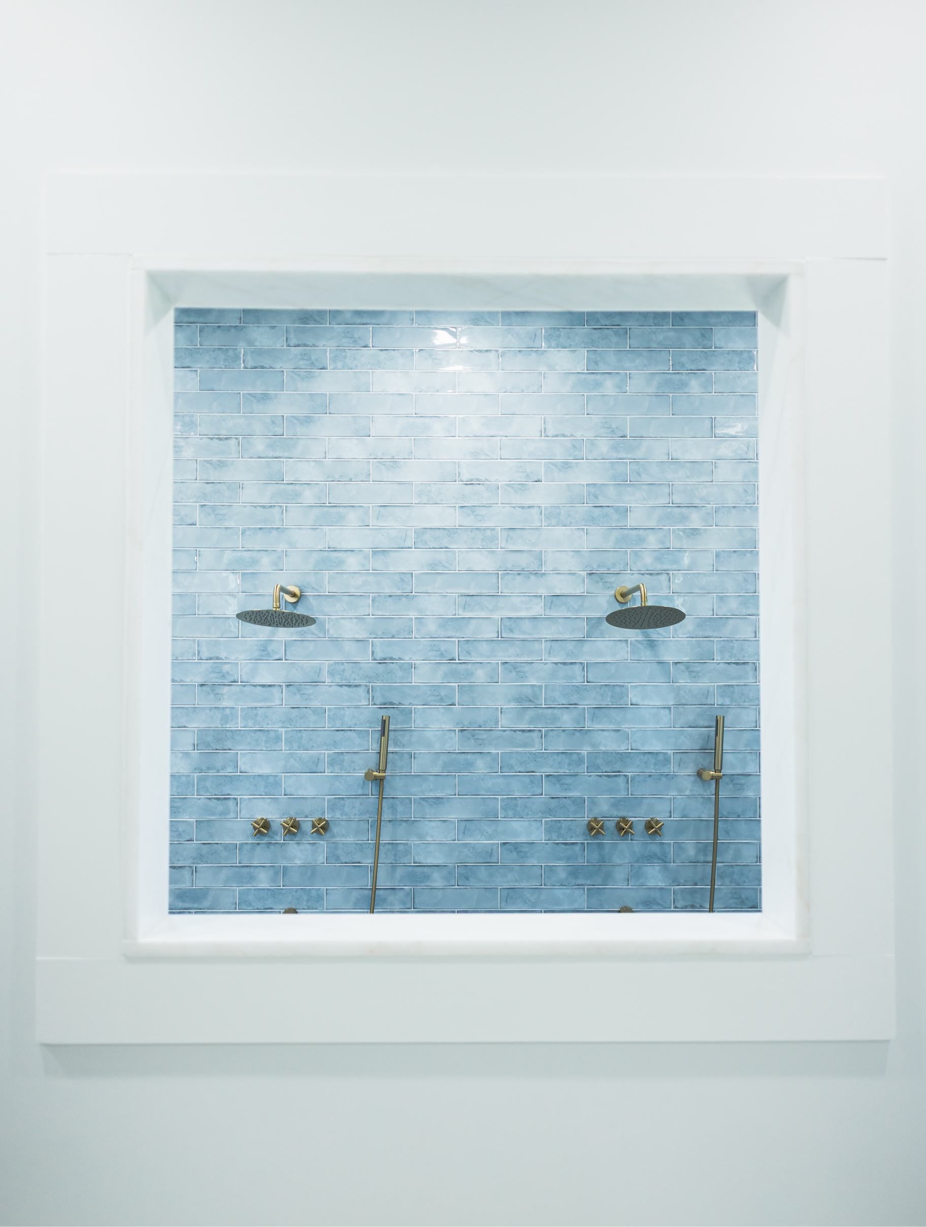 Tiled shower stall with two showerheads and glass shelves, framed by white trim.