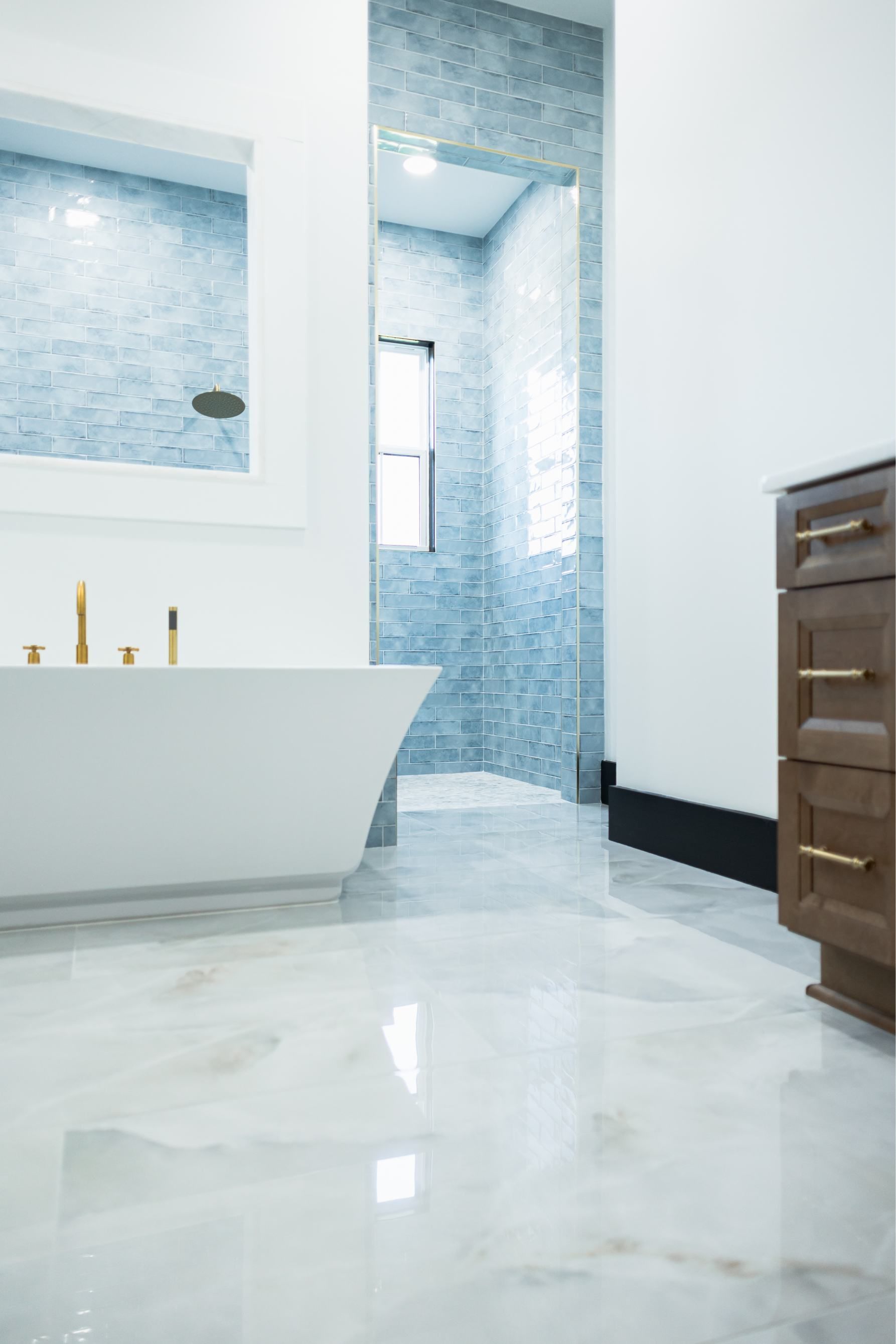 Modern bathroom with a freestanding tub, marble floor, and blue-tiled shower area