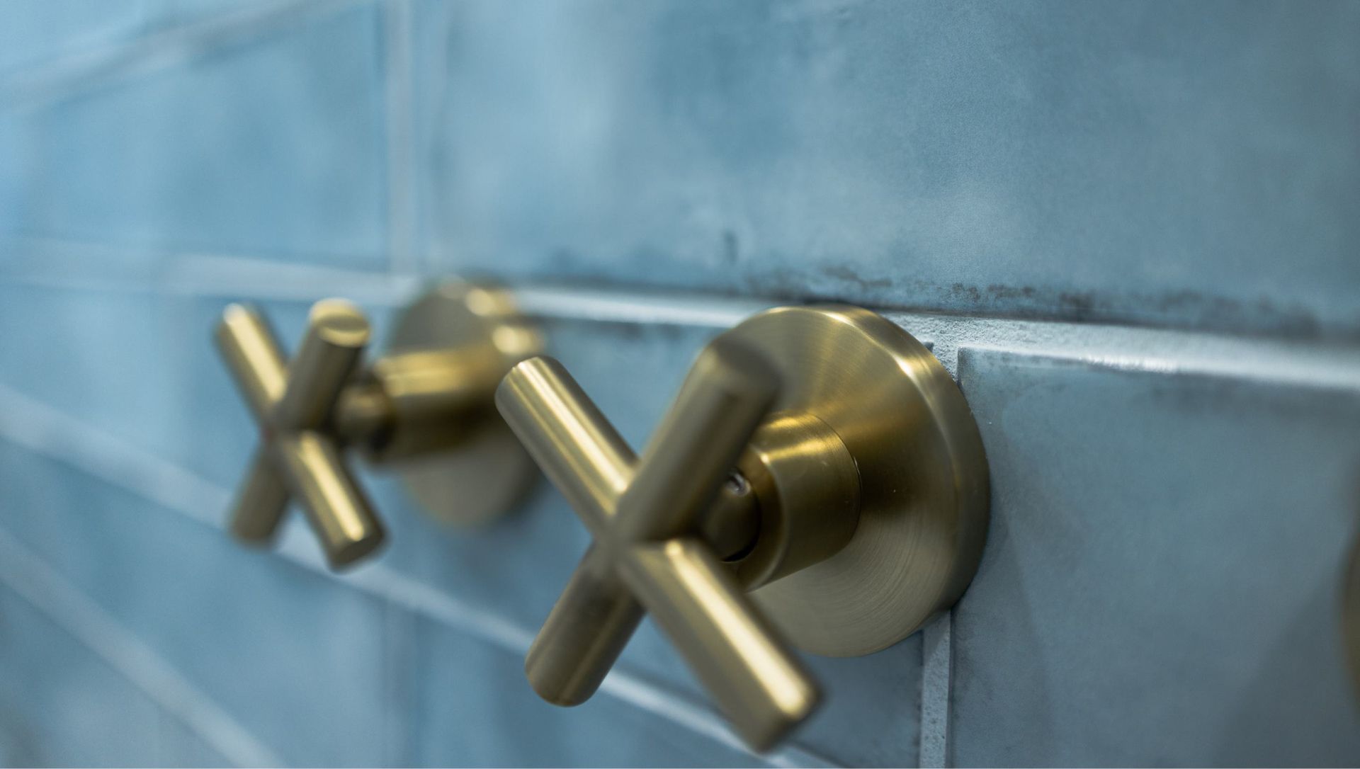 Two brass cross-handle faucets mounted on a blue tiled wall.