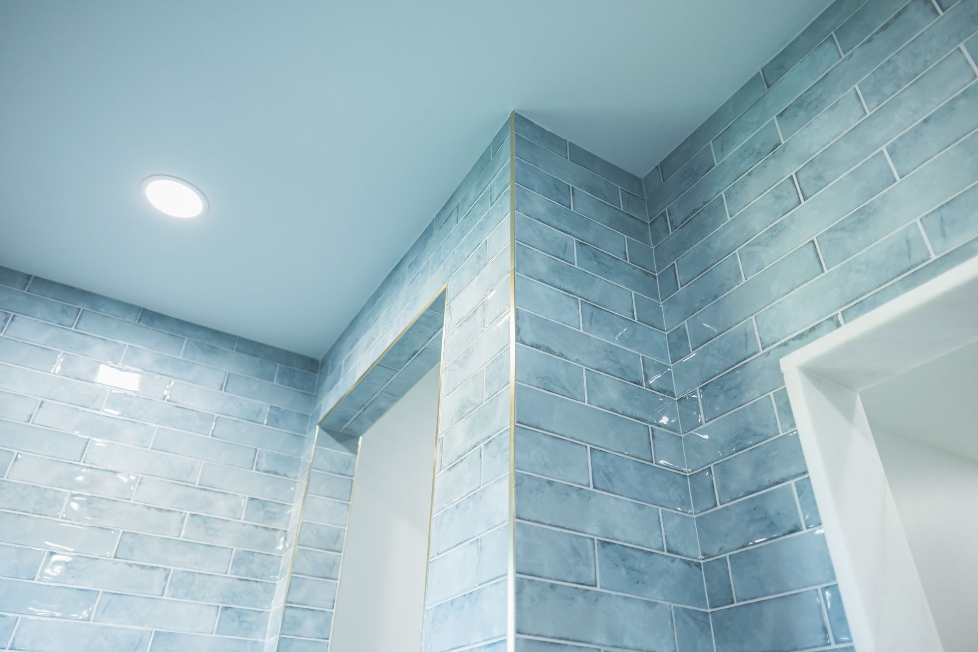 Light blue tiled bathroom ceiling and walls with recessed lights and white door frames