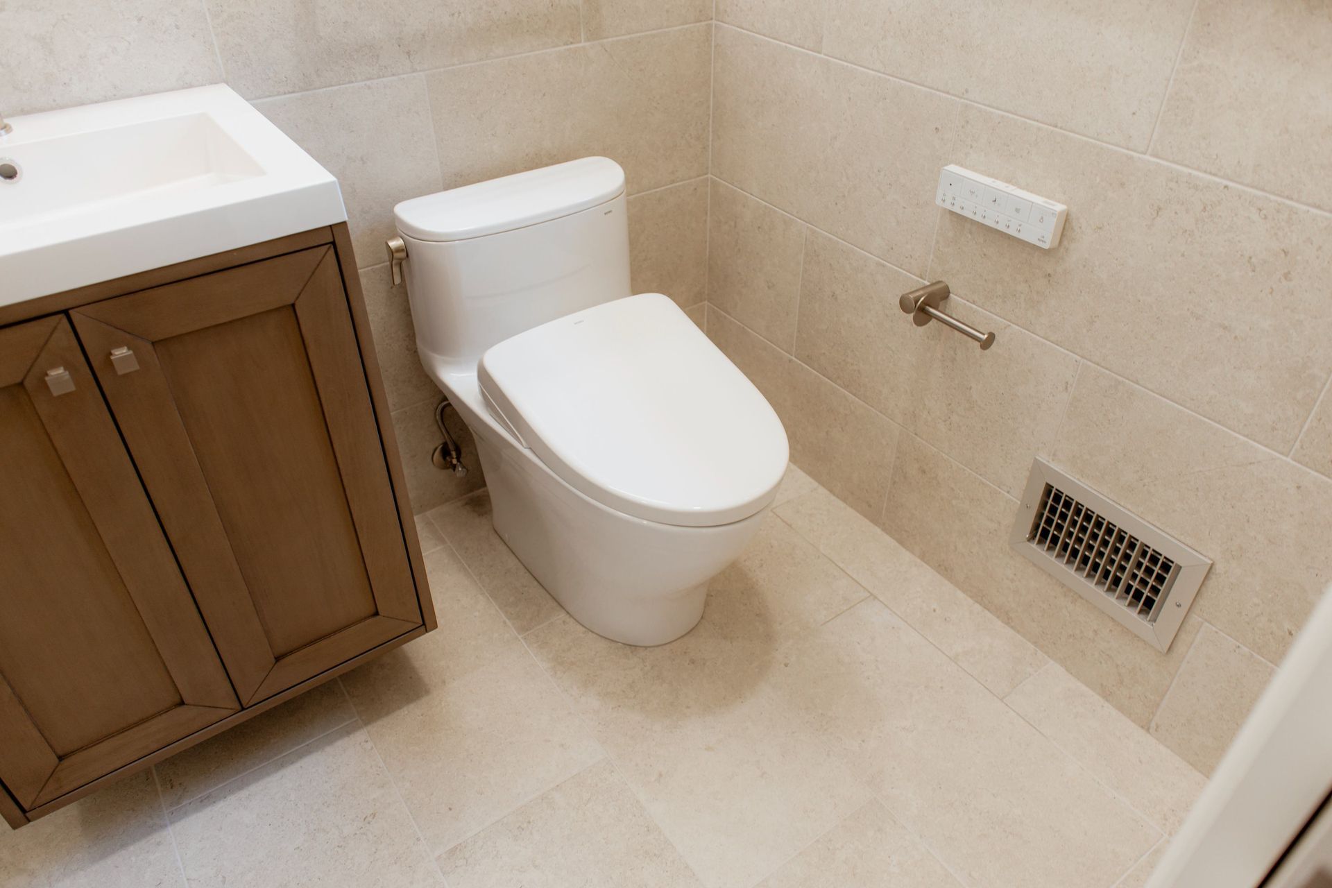 Modern bathroom with white toilet, beige tile walls and floor, and wood vanity sink cabinet