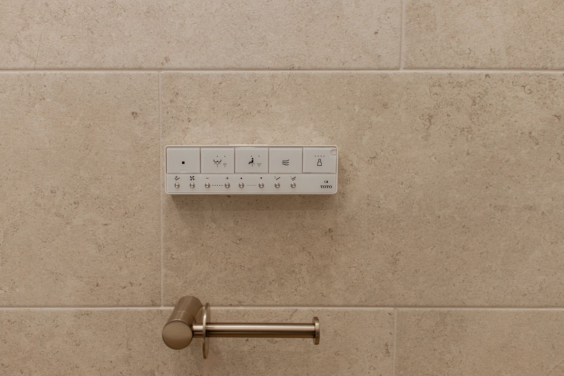 Bathroom wall with tiled backdrop, control panel, and a mounted toilet paper holder.