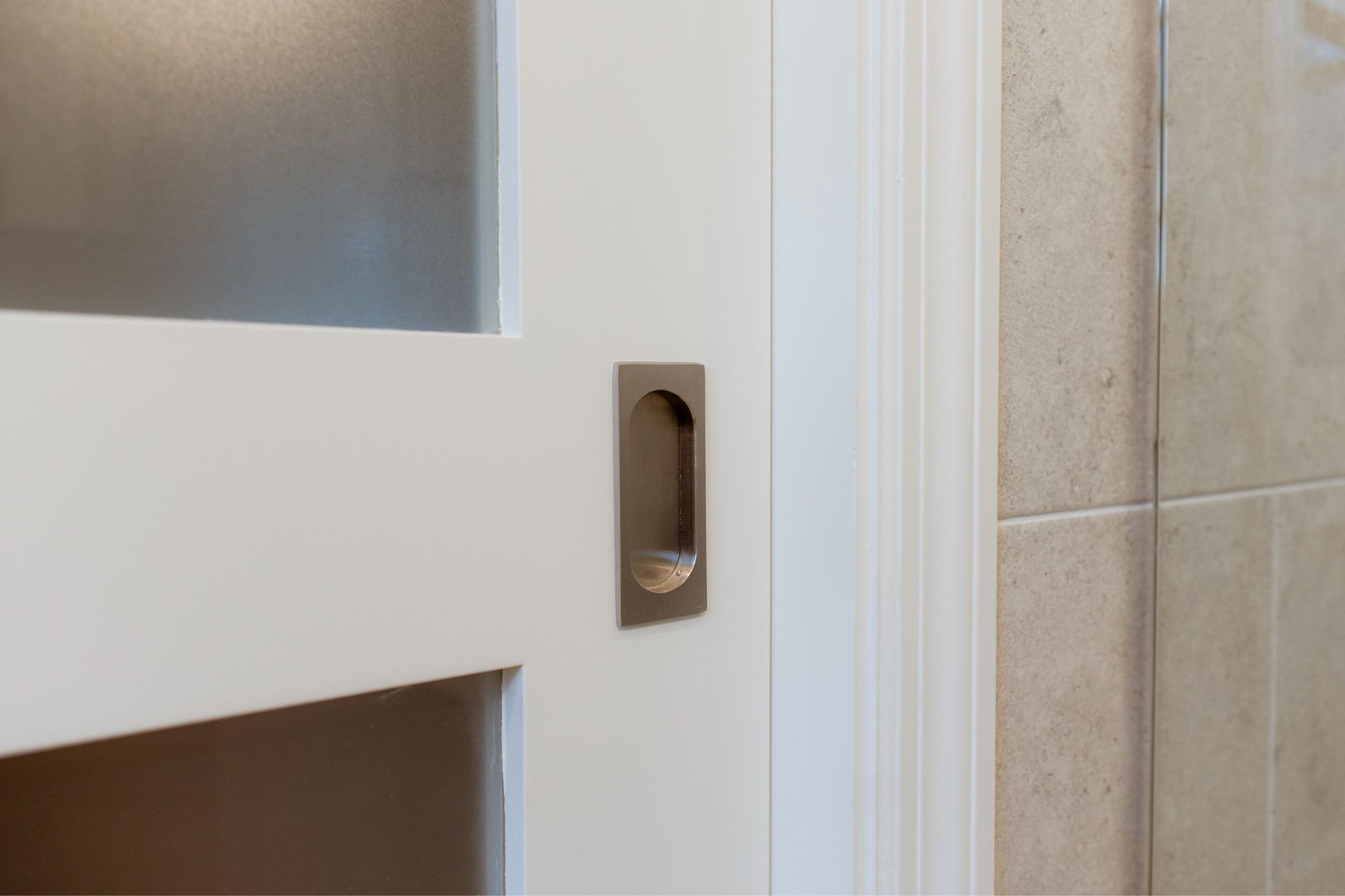 Close-up of a white door handle beside beige tiled wall and frosted glass panel