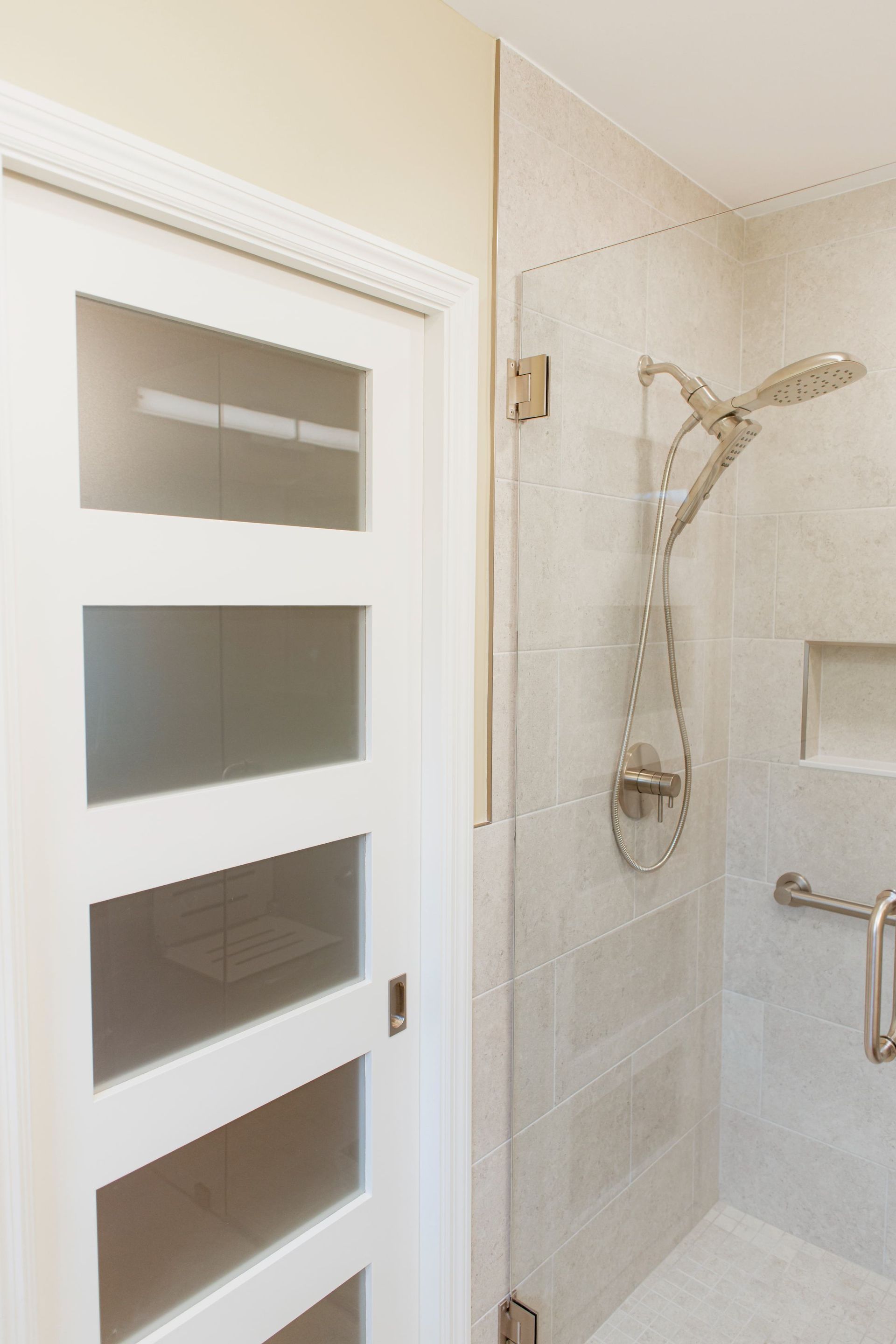 Walk-in shower with light tile walls, handheld showerhead, and frosted glass door with rectangular panes