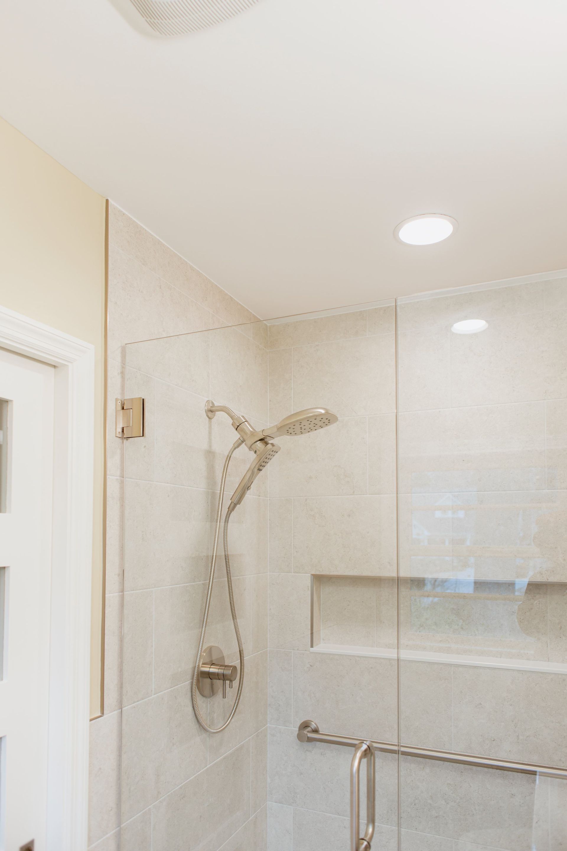 Modern shower with glass enclosure, rainfall showerhead, and beige tile walls