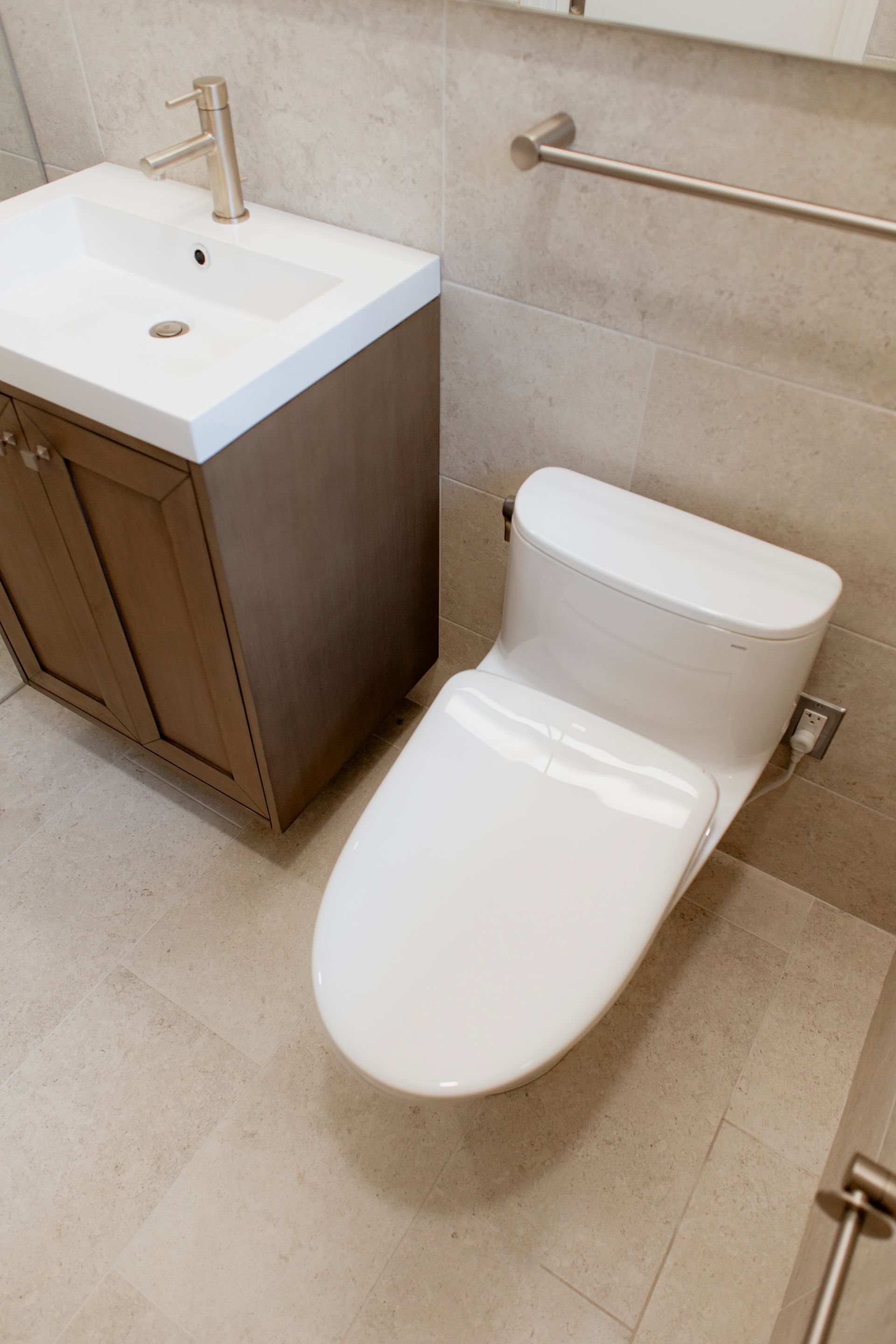 Modern bathroom with a white sink cabinet and a white toilet on beige tile floor.