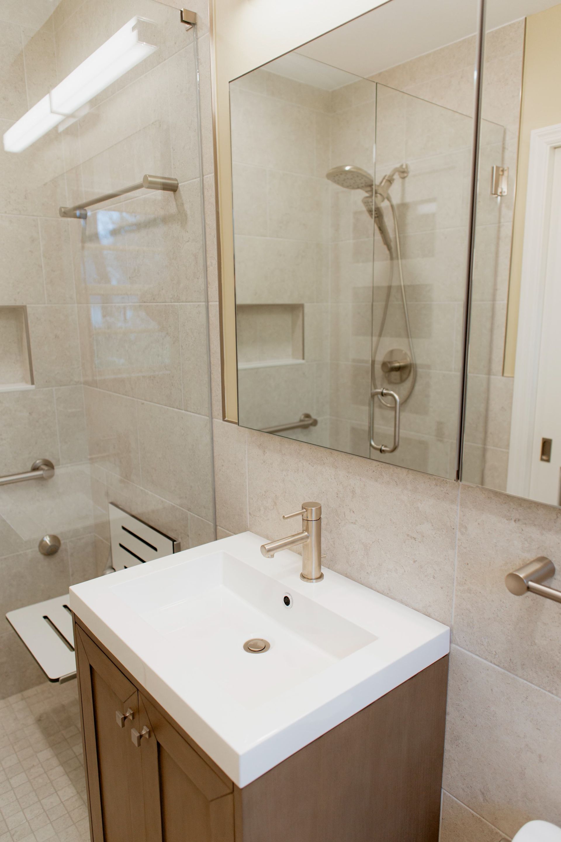 Modern bathroom vanity with white sink, large mirror, and glass shower in beige tile.