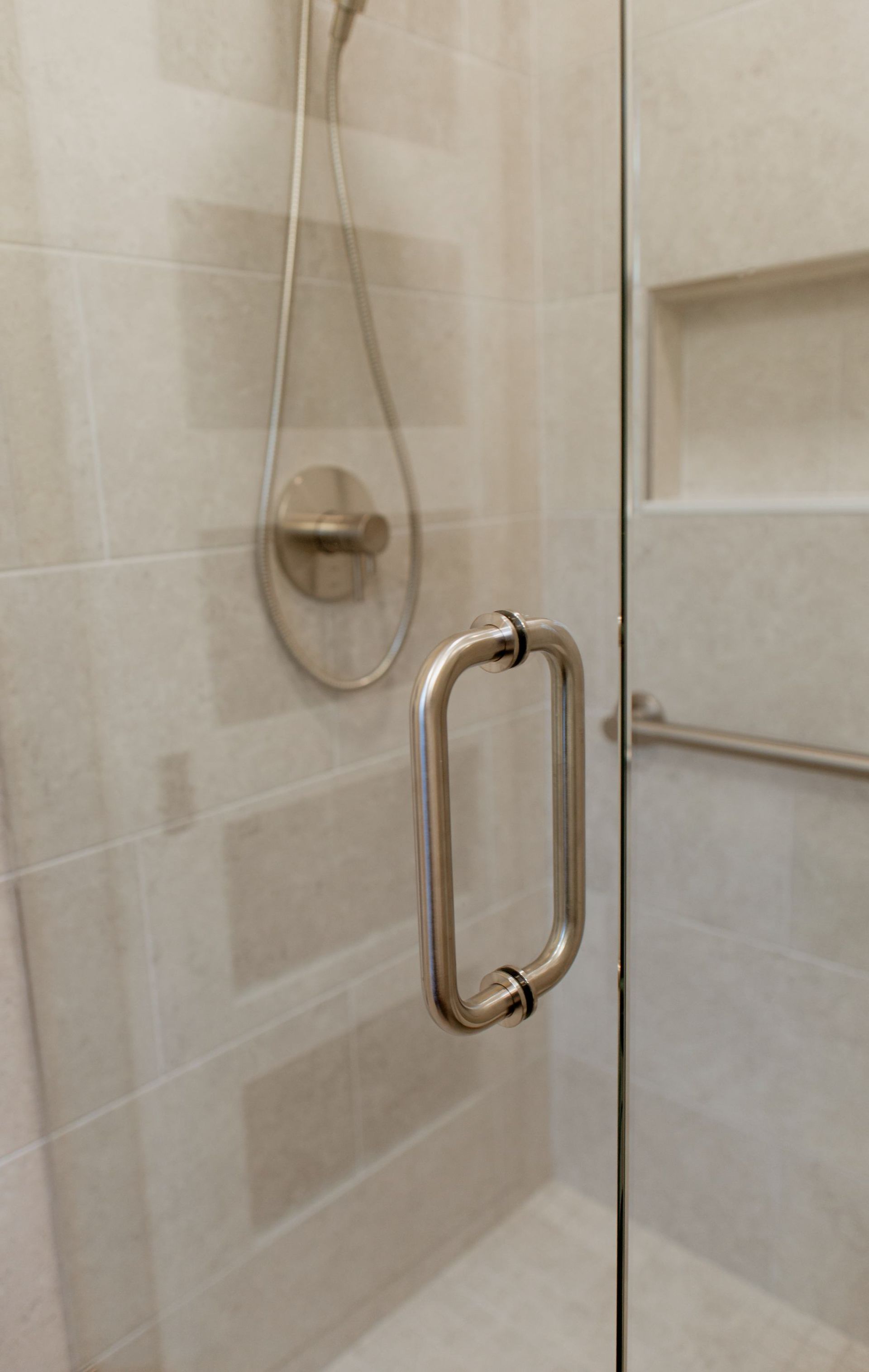 Glass shower door with chrome handle and beige tiled shower interior