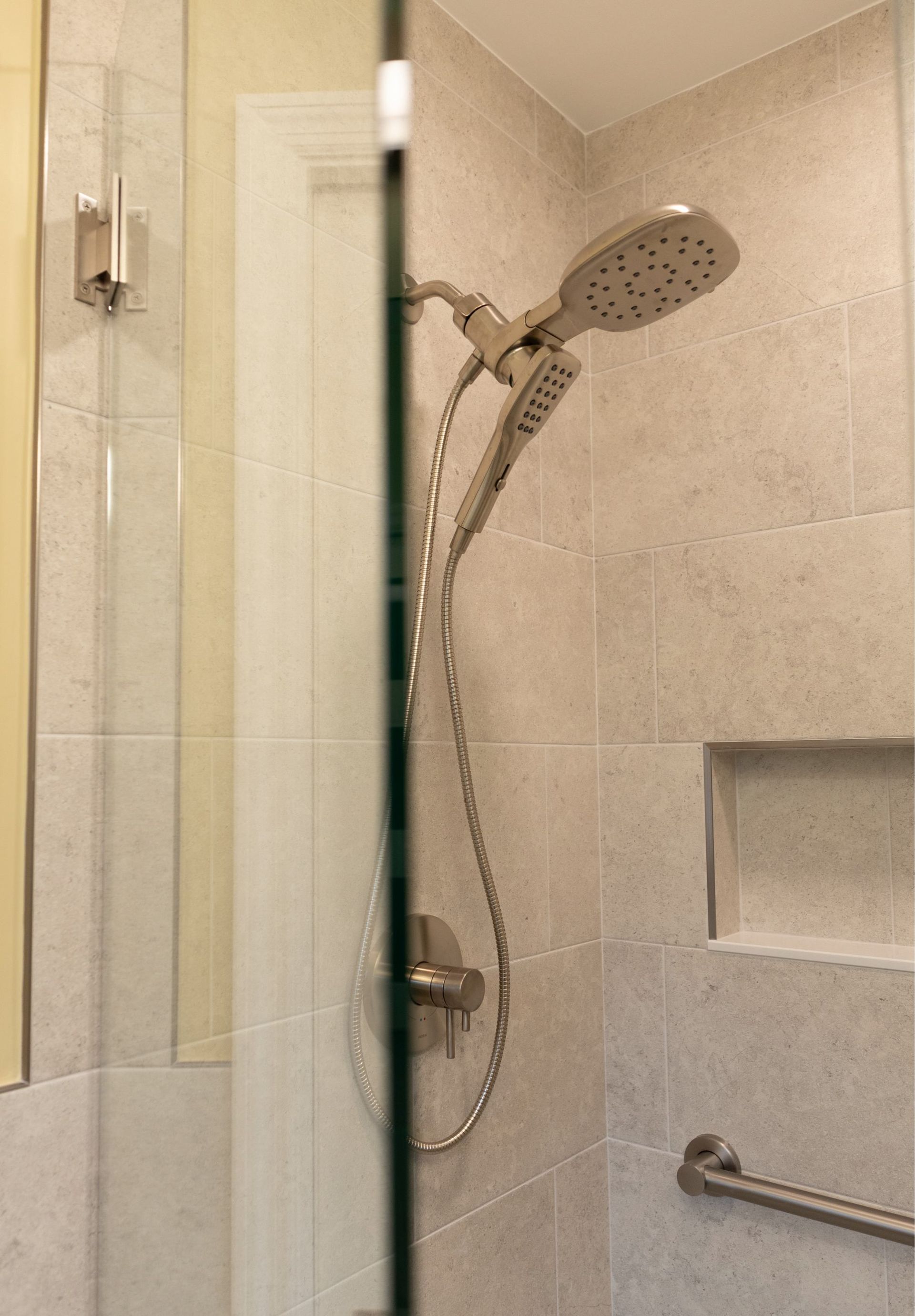 Shower stall with handheld showerhead, glass partition, and wall-mounted grab bar in a beige bathroom