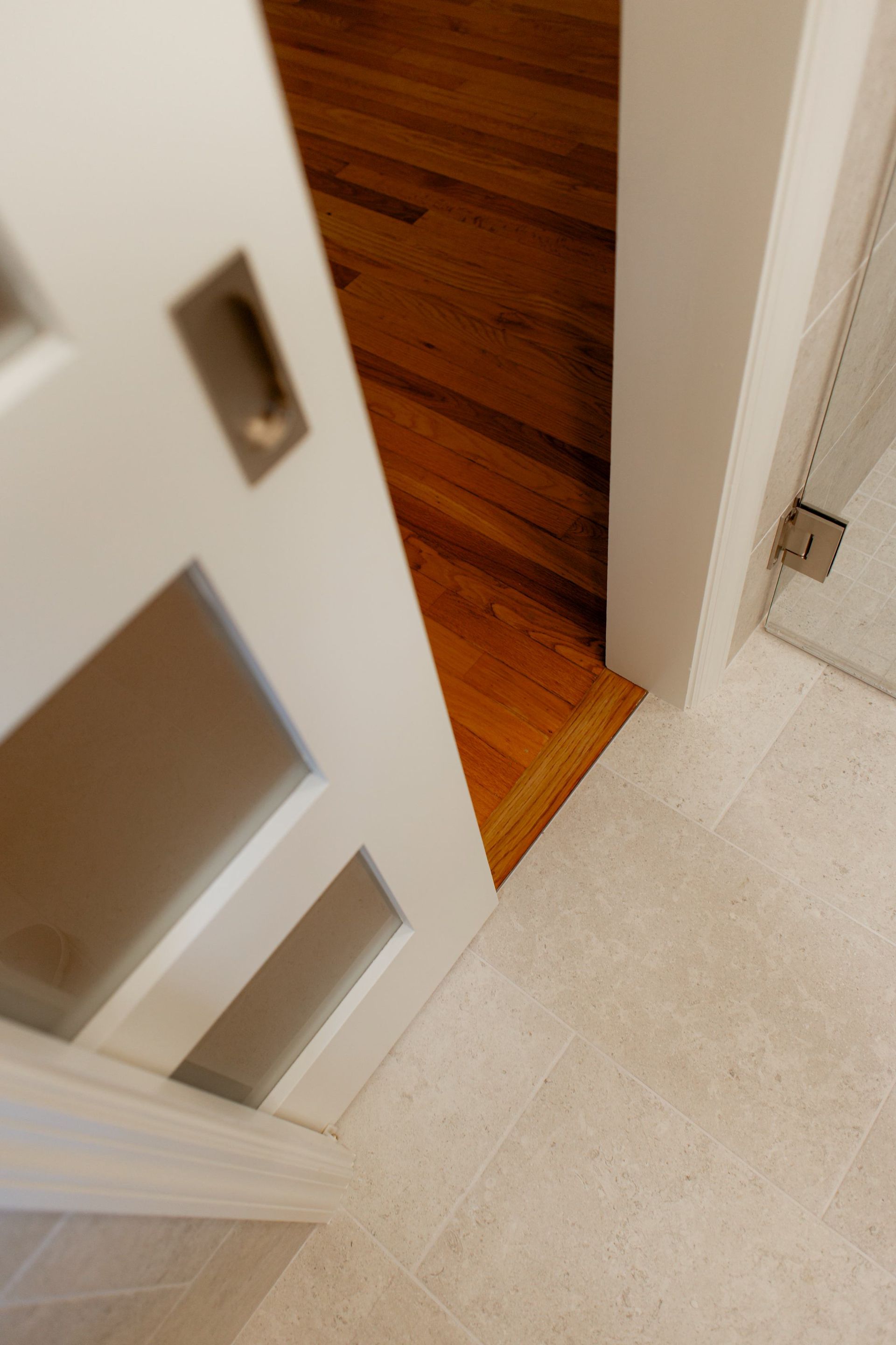 Partially open white door revealing a hardwood floor and tiled hallway entrance