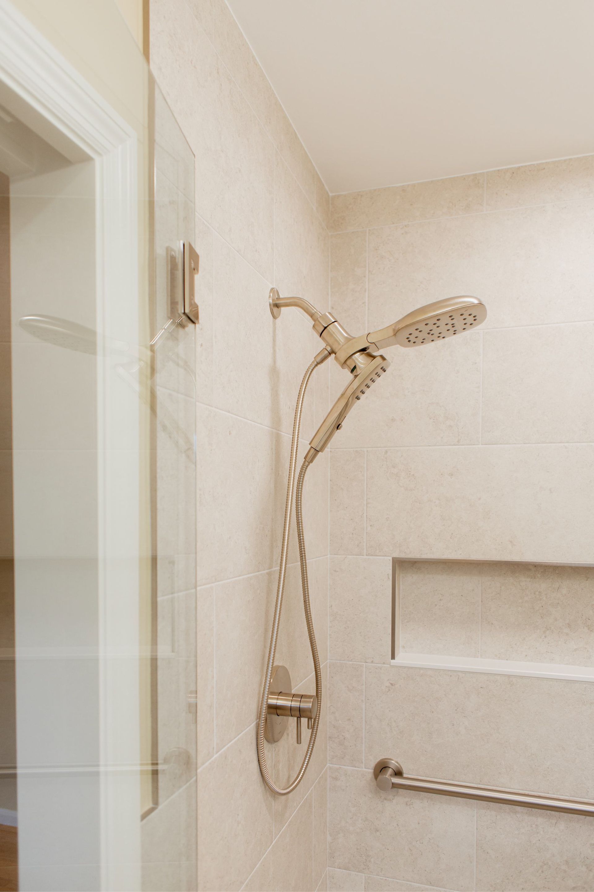 Bathroom shower with beige tile, handheld showerhead, and grab bar in a tiled stall