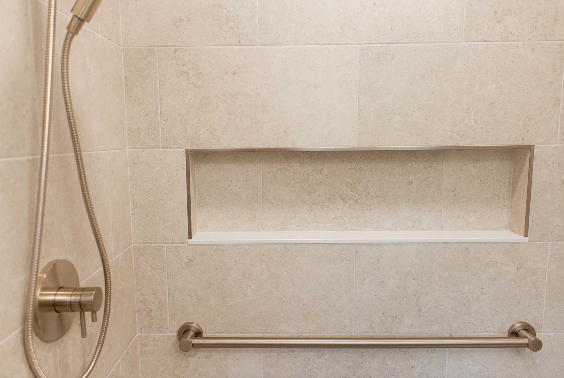Tiled bathroom shower with handheld showerhead, recessed shelf, and chrome grab bar