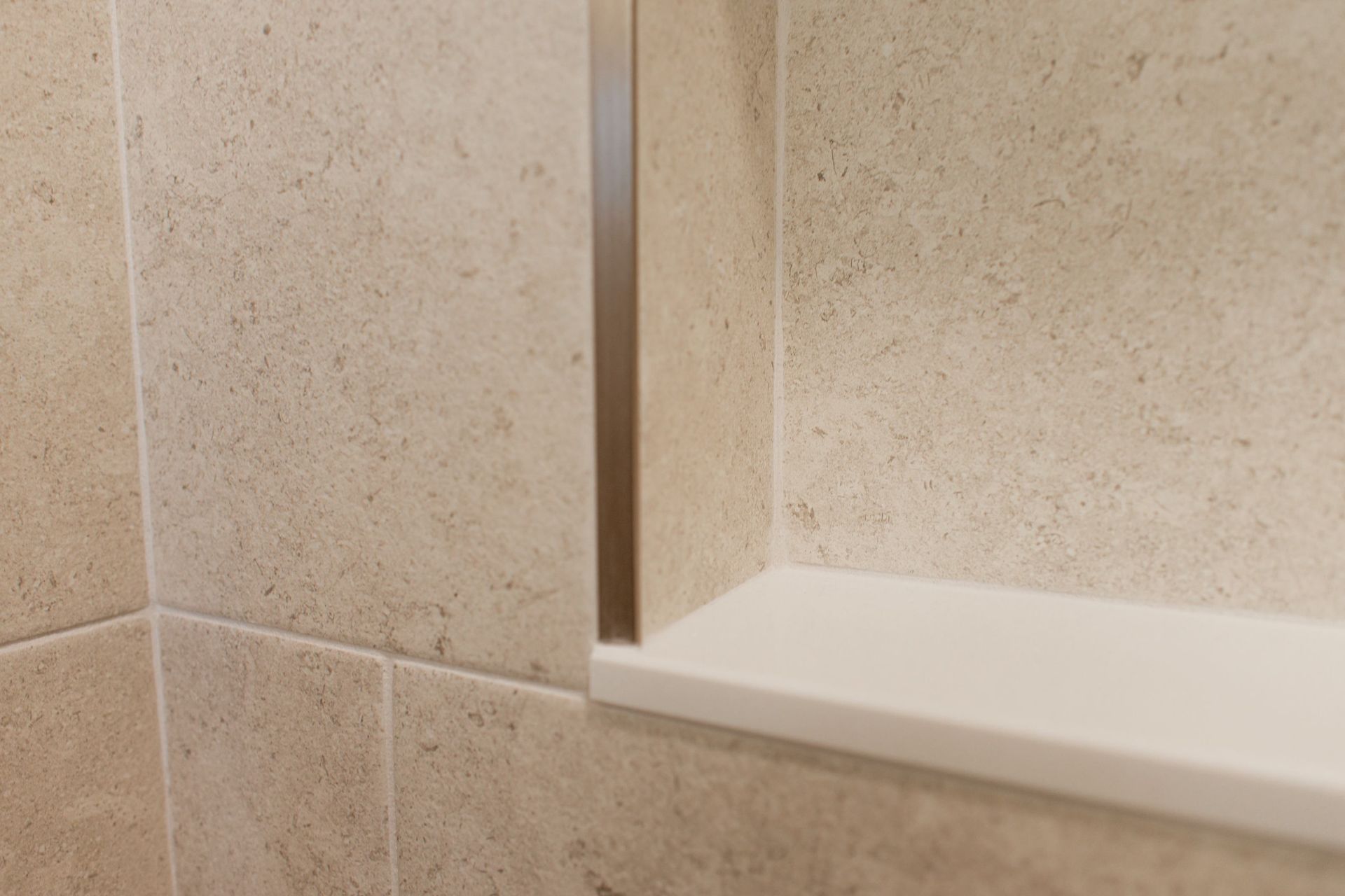 Beige tiled shower corner with a white corner shelf and vertical glass panel