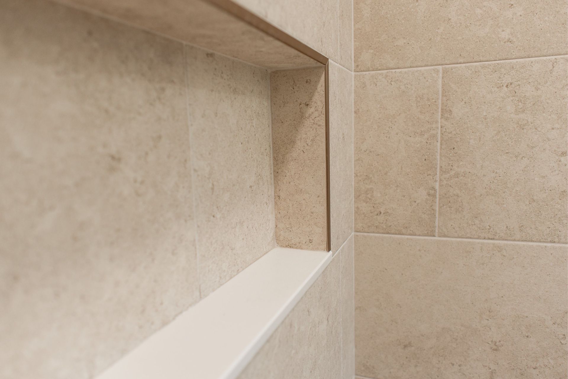 Tiled shower corner with a white built-in bench and beige stone walls
