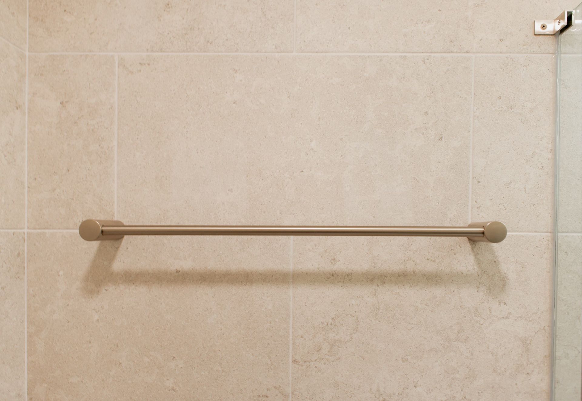 Beige tiled wall with a horizontal towel bar and small fixture in the upper right corner