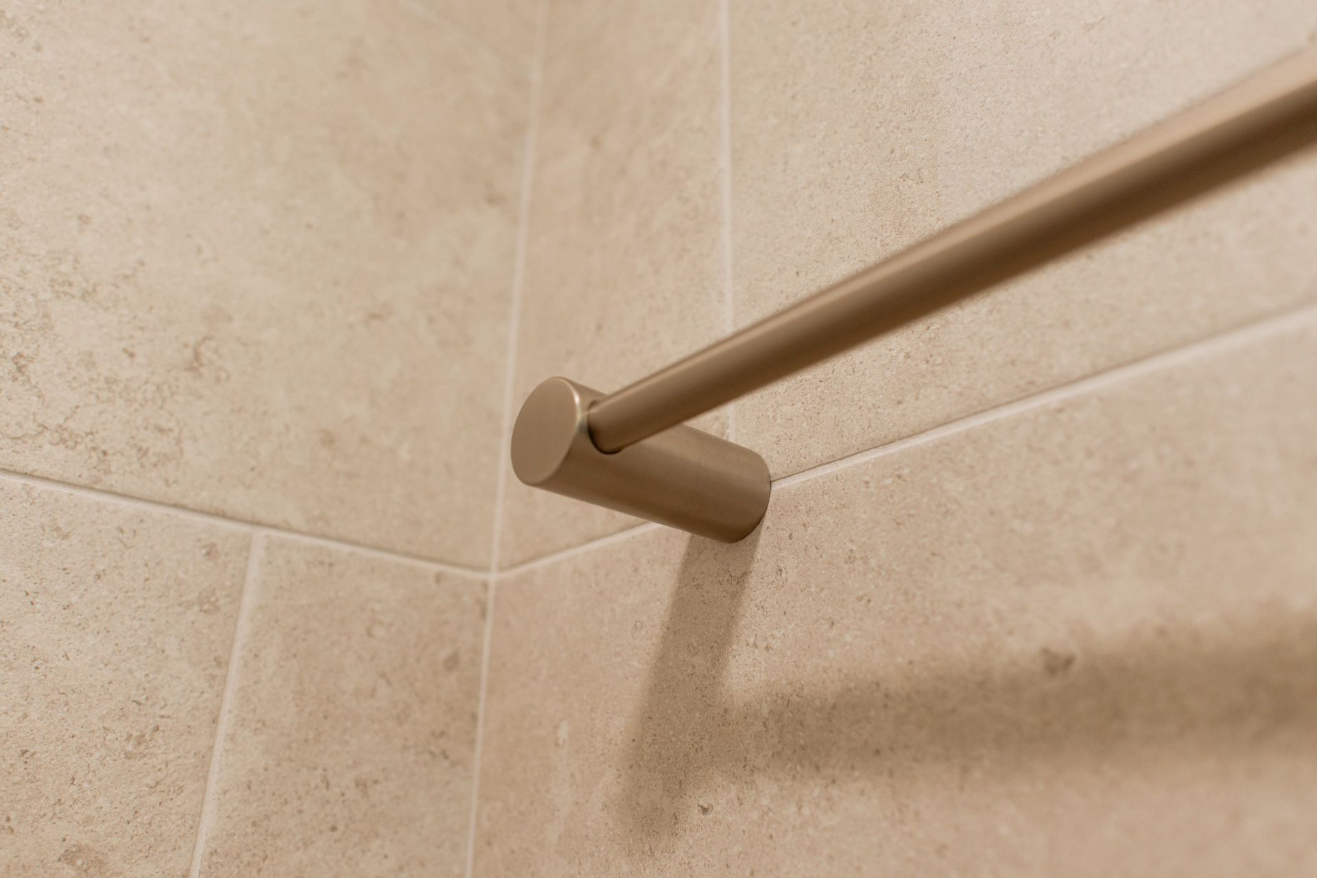 Tan grab bar mounted on beige tiled shower wall