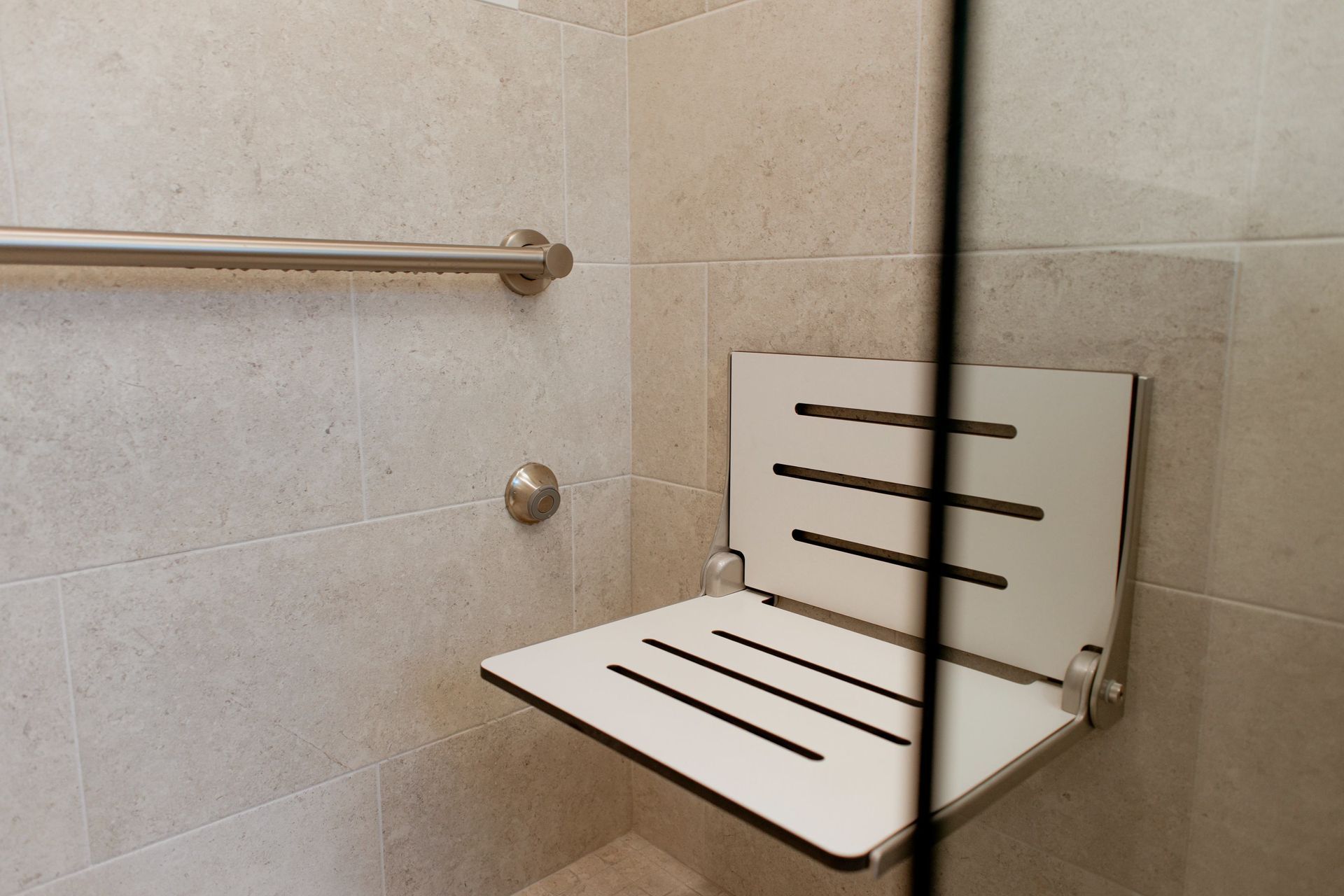 Fold-down shower seat with white slatted back and seat in a tiled bathroom stall.