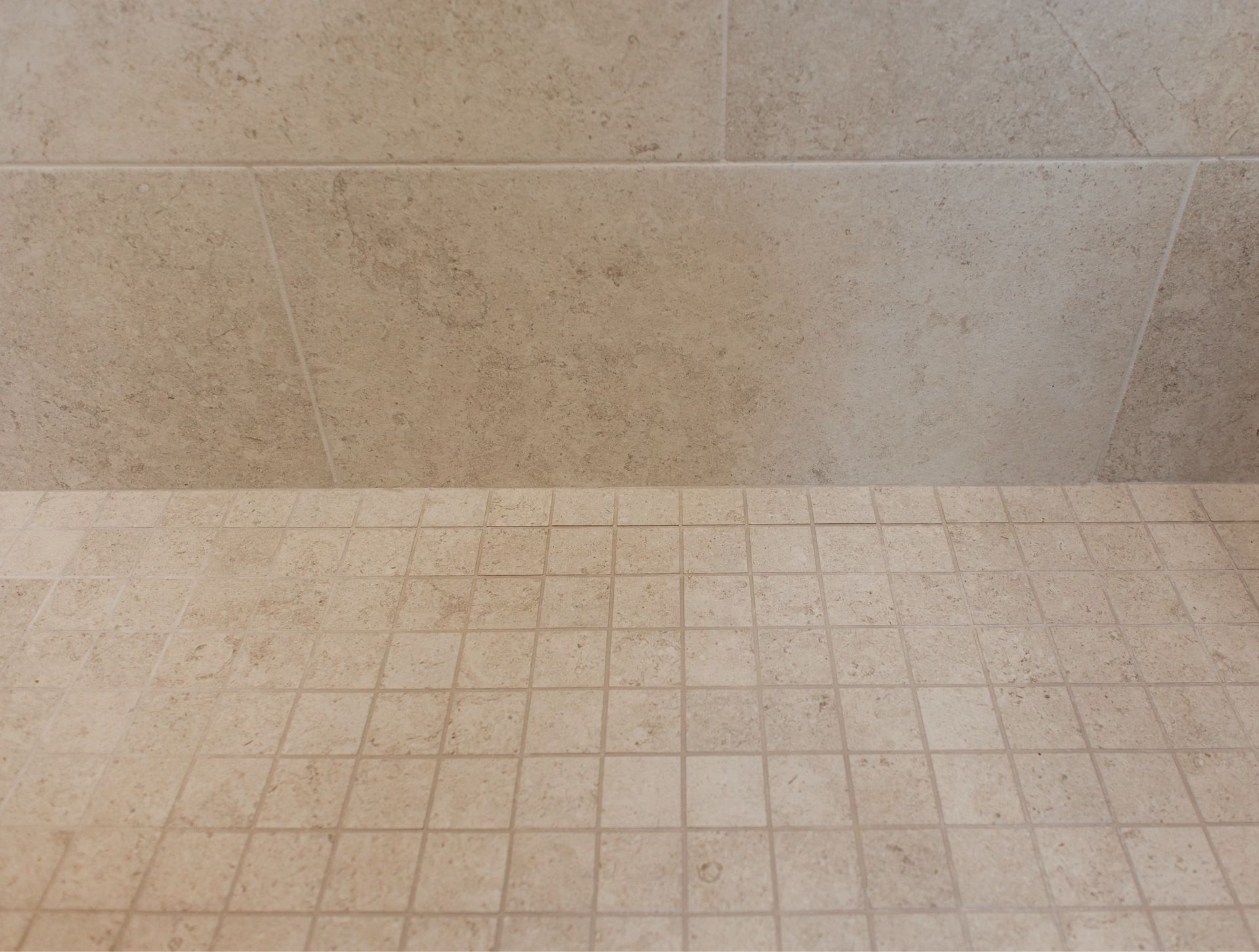 Beige tiled wall and floor corner with light grout lines in a bathroom or shower area