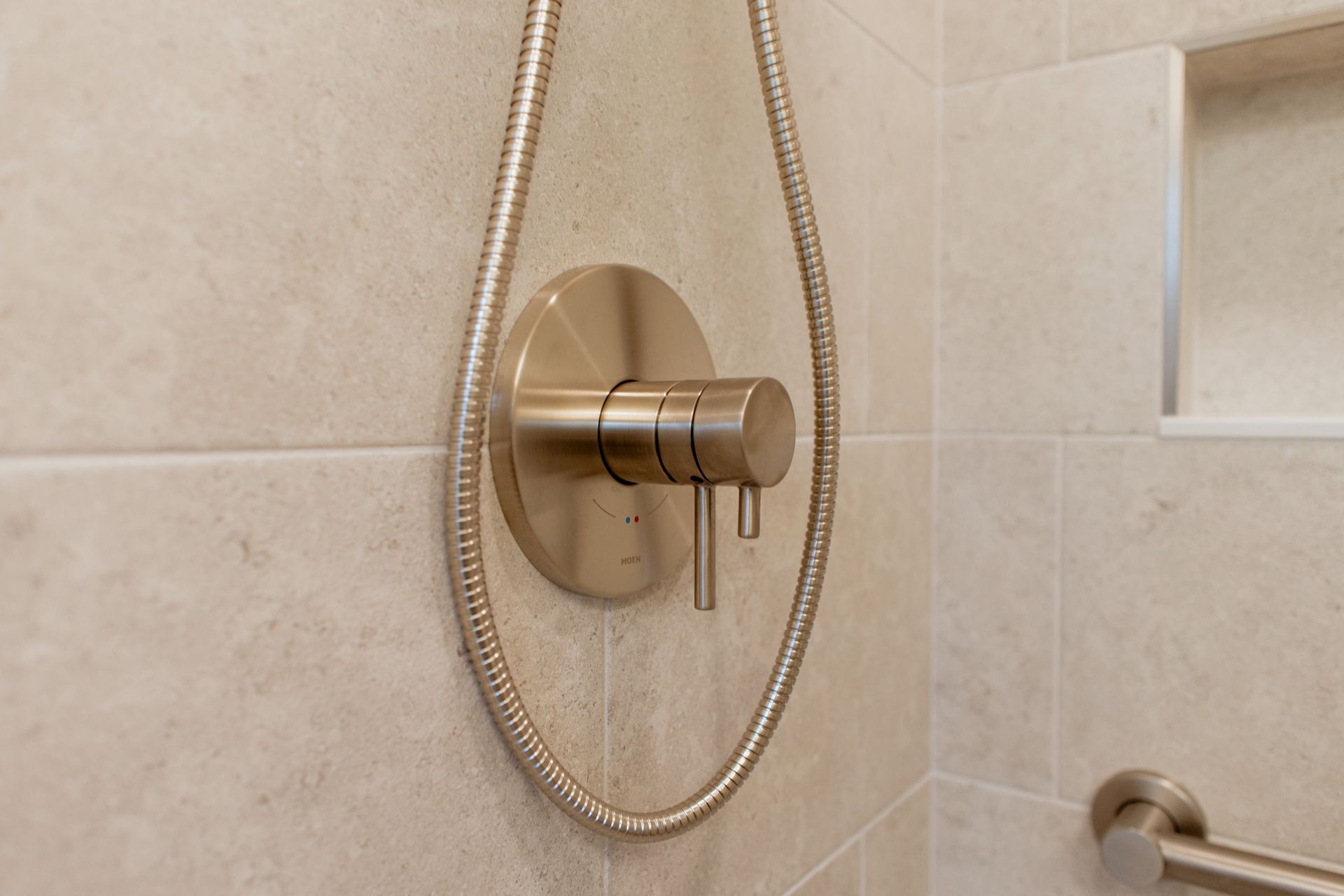 Brushed gold shower control and handheld showerhead on beige tiled bathroom wall