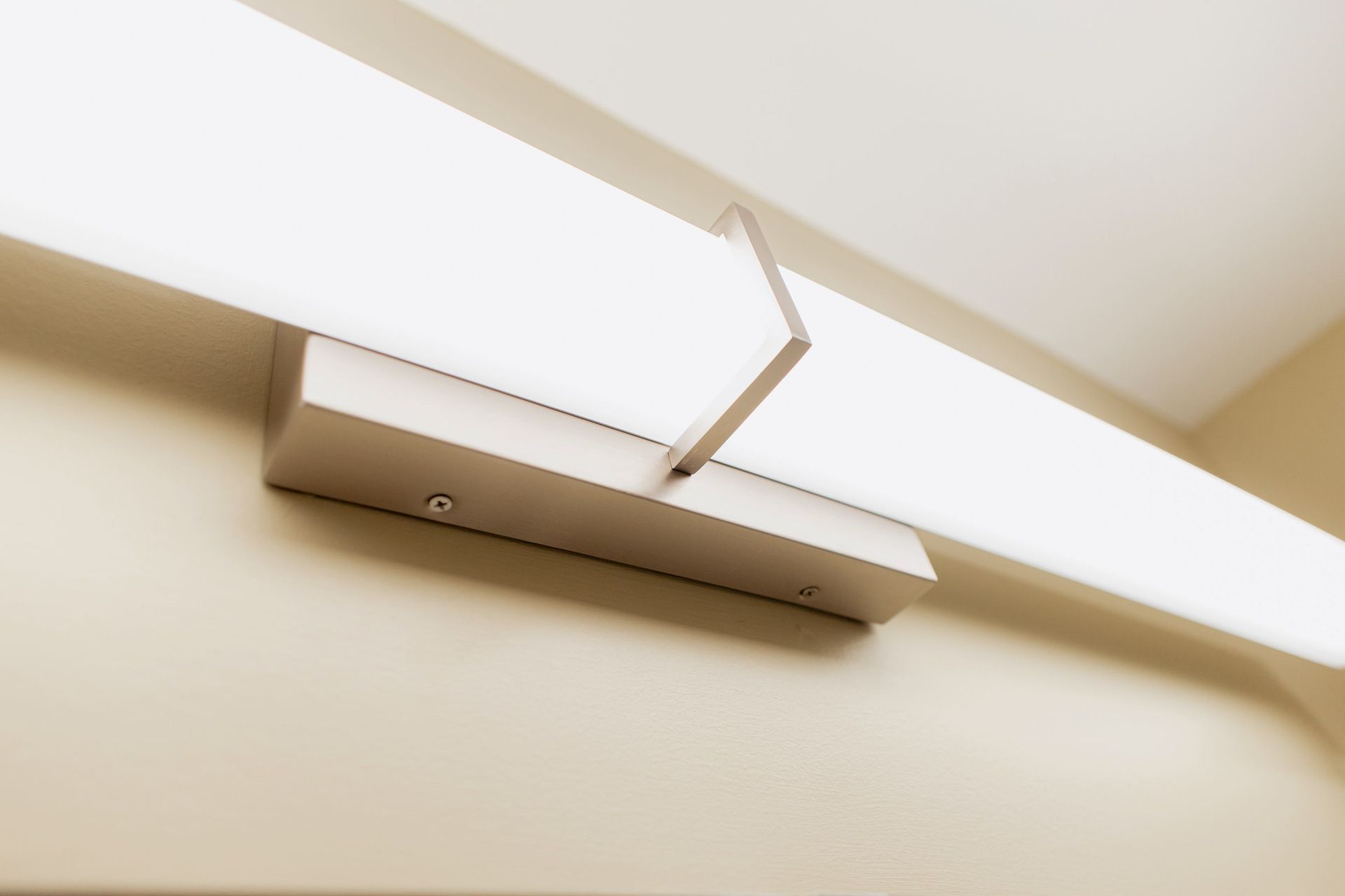 Wall-mounted beige door closer on a light-colored wall ceiling junction.