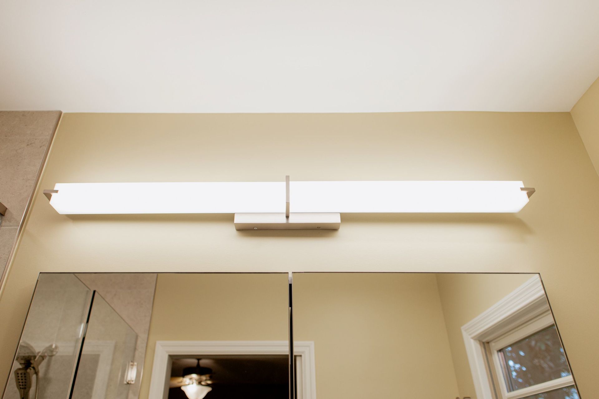 Bathroom vanity light above mirror with a white shade and beige walls