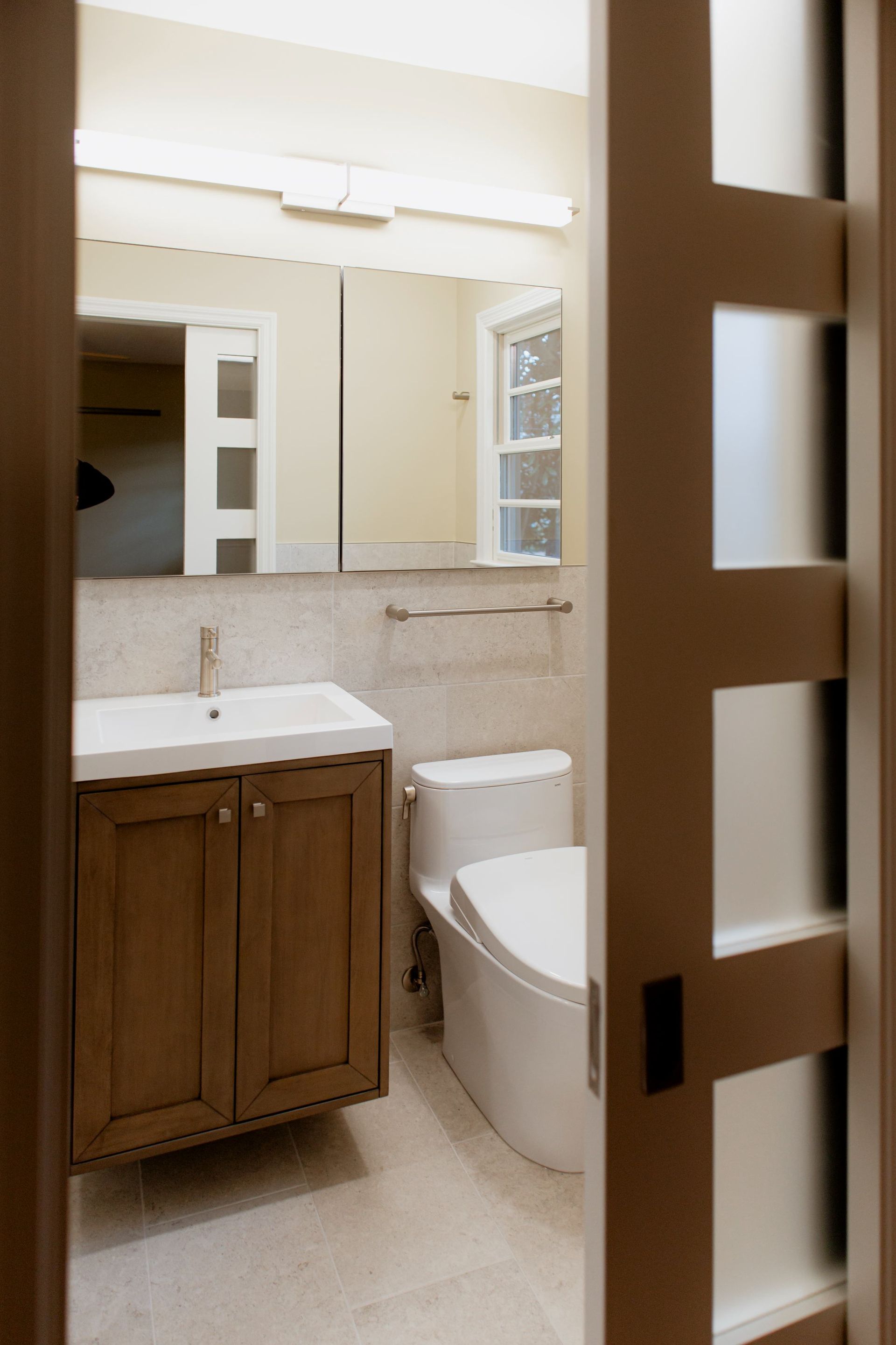 Small bathroom with sink, toilet, and shower, viewed through a sliding door with frosted glass panels.