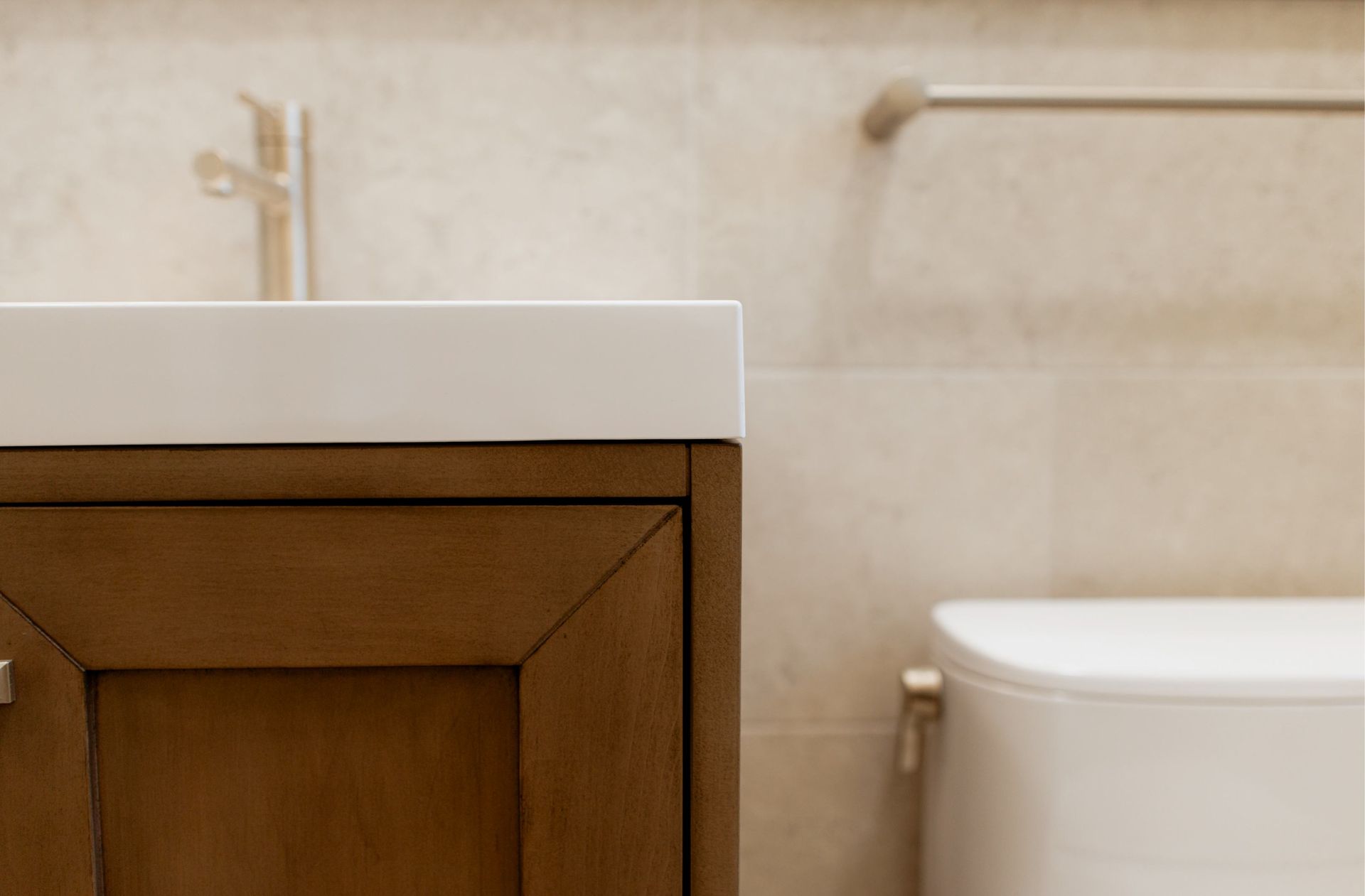Bathroom vanity with white sink, wooden cabinet, and part of a white bathtub in a beige tiled room