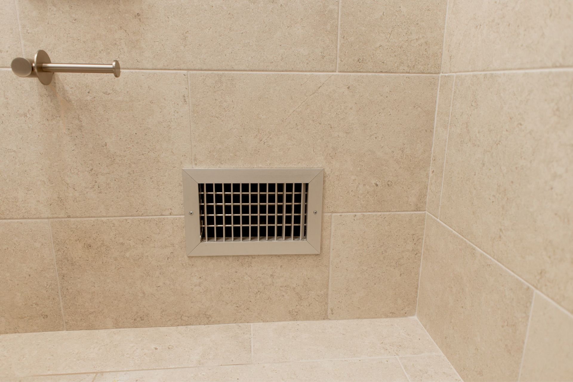 Beige tiled shower wall with a central vent and a metal towel bar on the left
