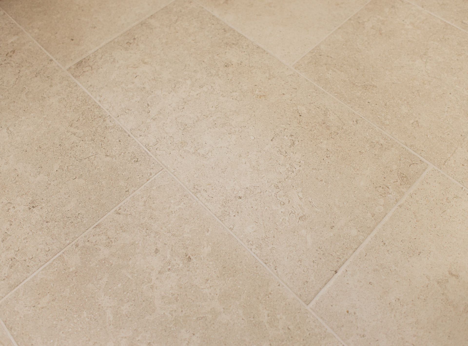 Close-up of beige tiled floor with subtle diagonal grout lines and light speckled texture