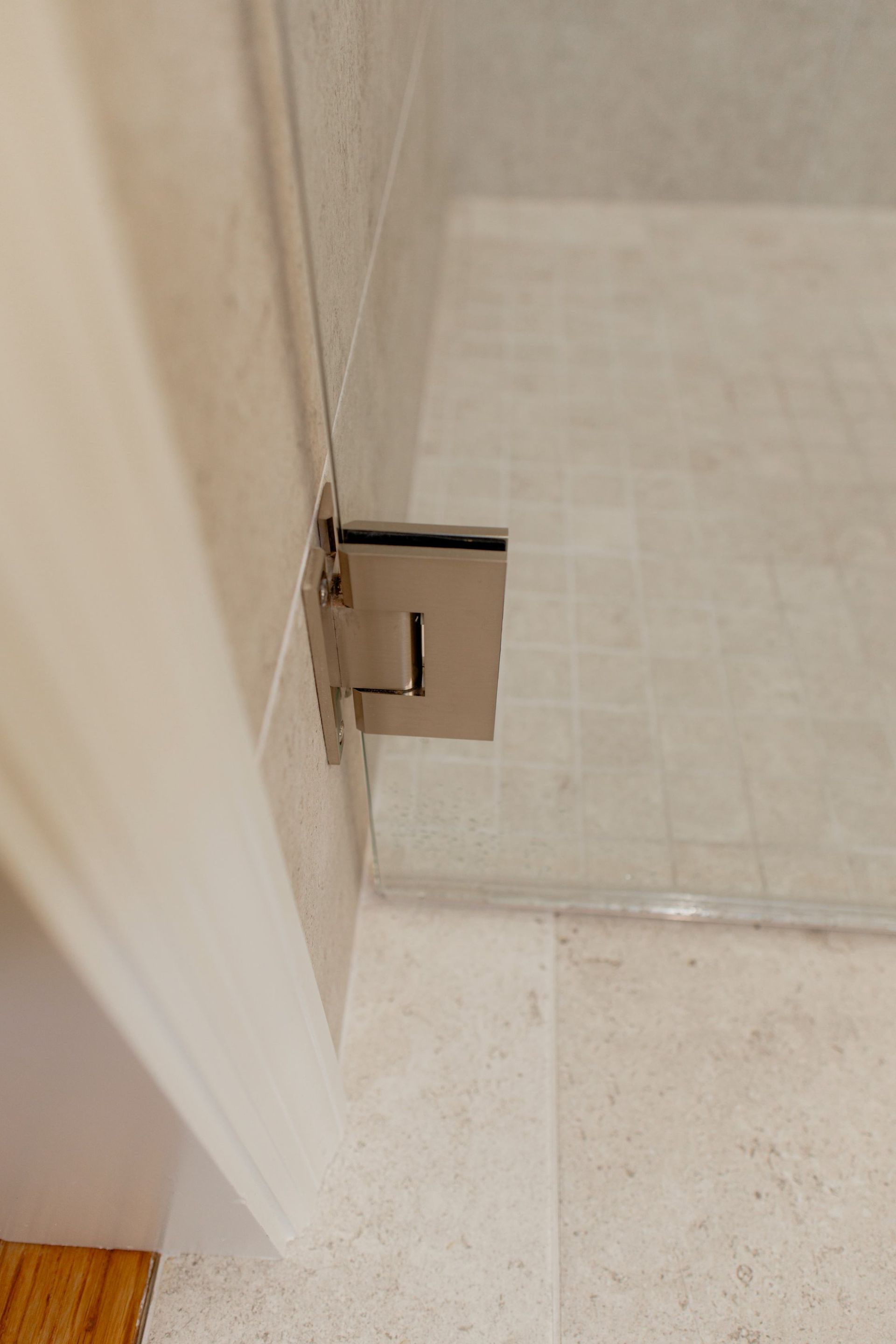 Close-up of a shower door hinge and latch on a beige tiled bathroom wall