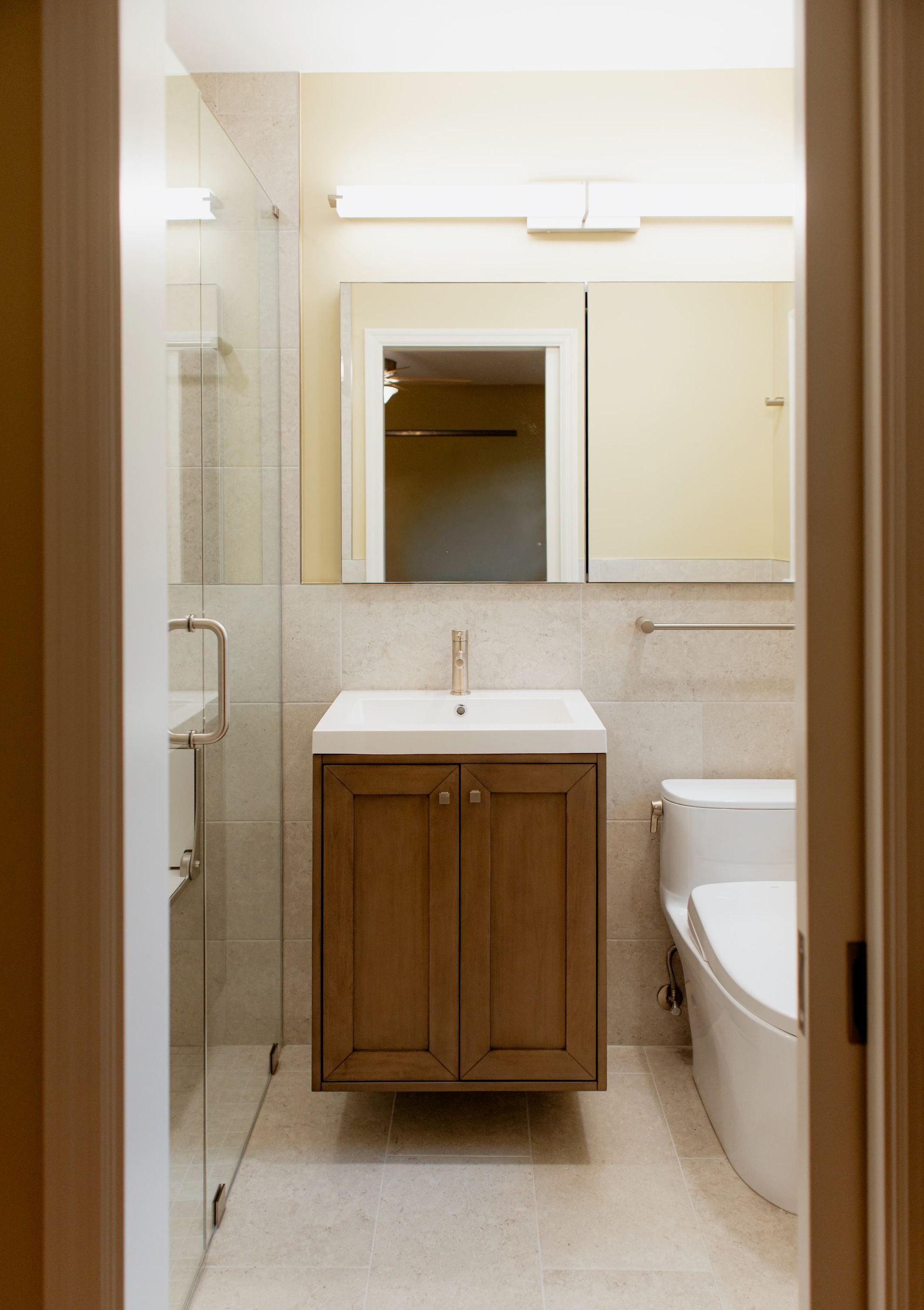 Small bathroom with sink, mirror, and toilet beside a bathtub, in neutral beige tones.