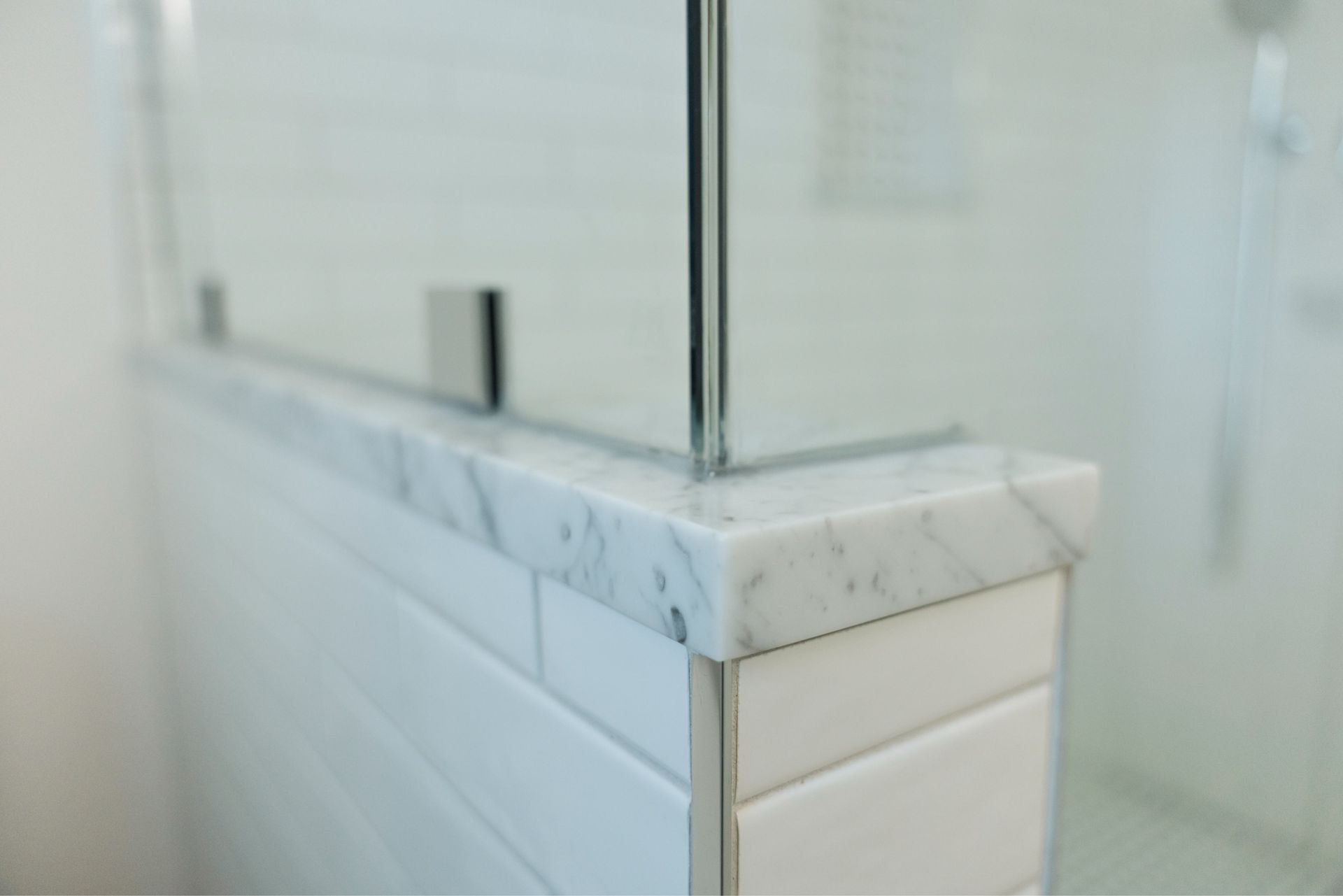 Marble shower ledge with glass door and white tiled wall in a bathroom