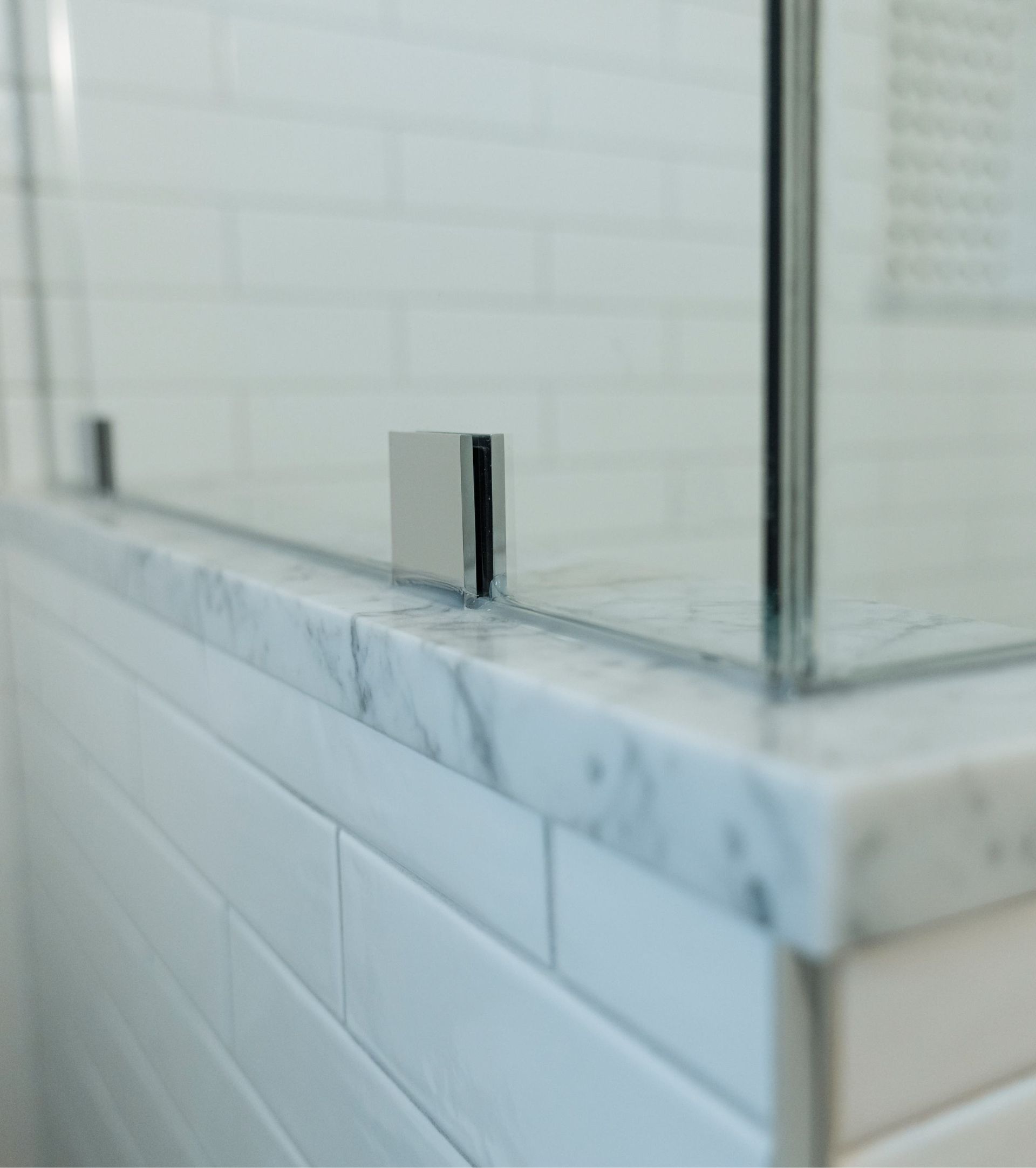 Glass shower enclosure with chrome trim over white marble tile and trim