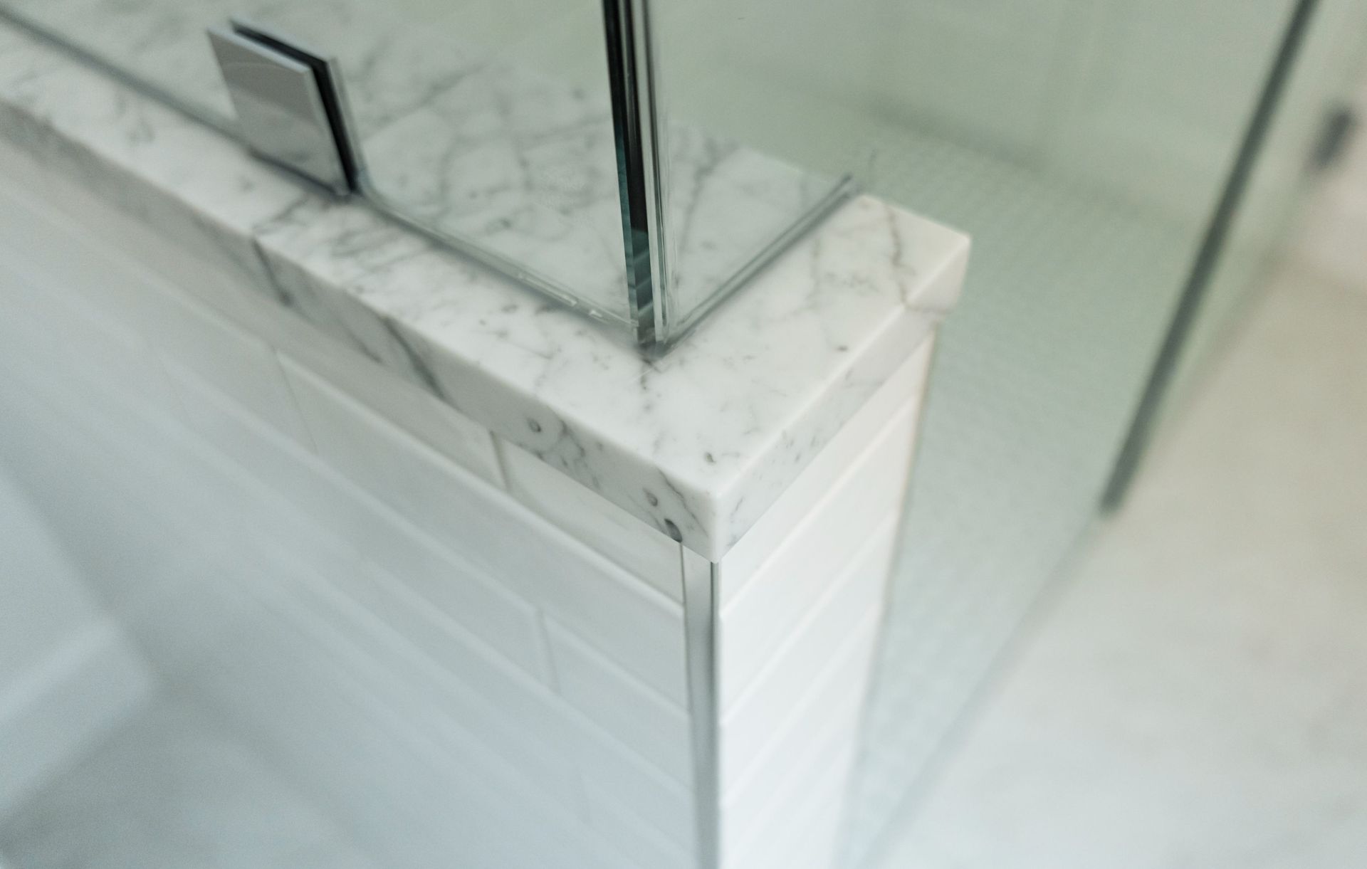 Glass shower corner with white marble tile trim and chrome frame