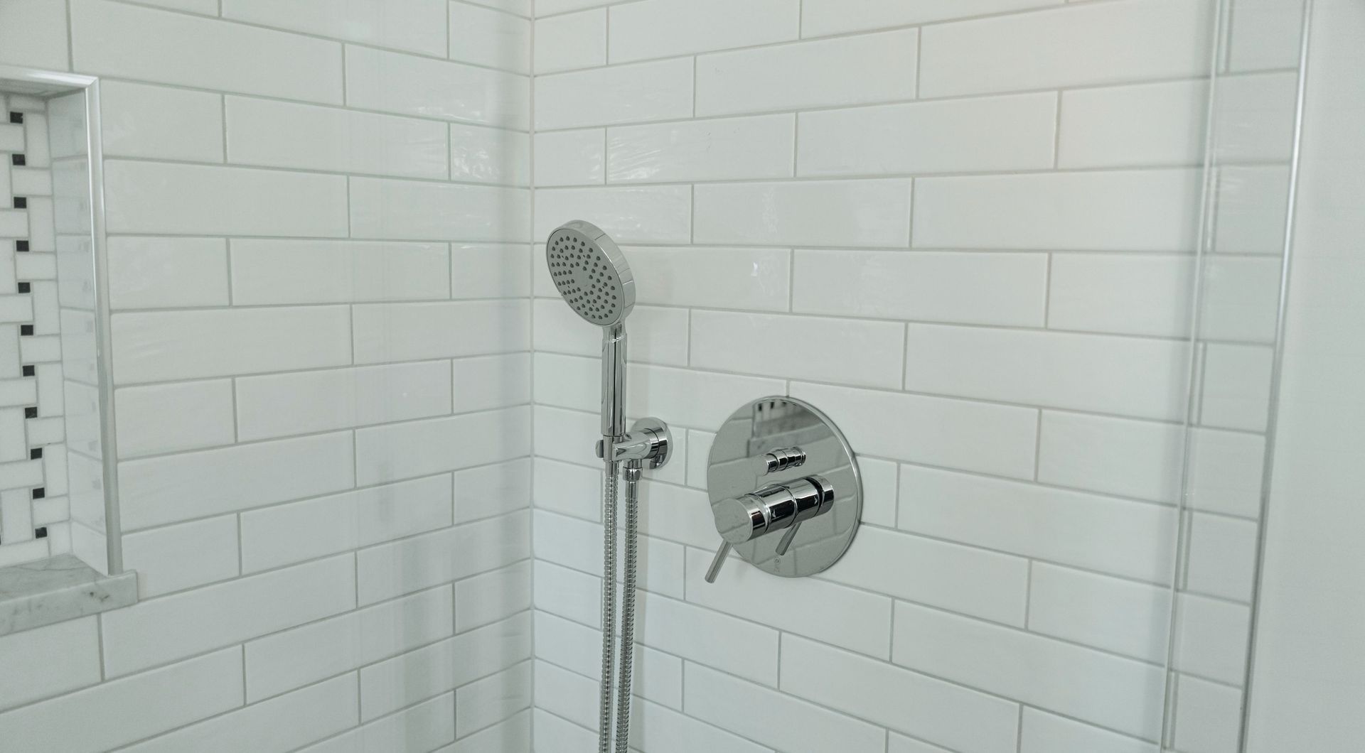 White tiled shower with handheld showerhead and chrome controls