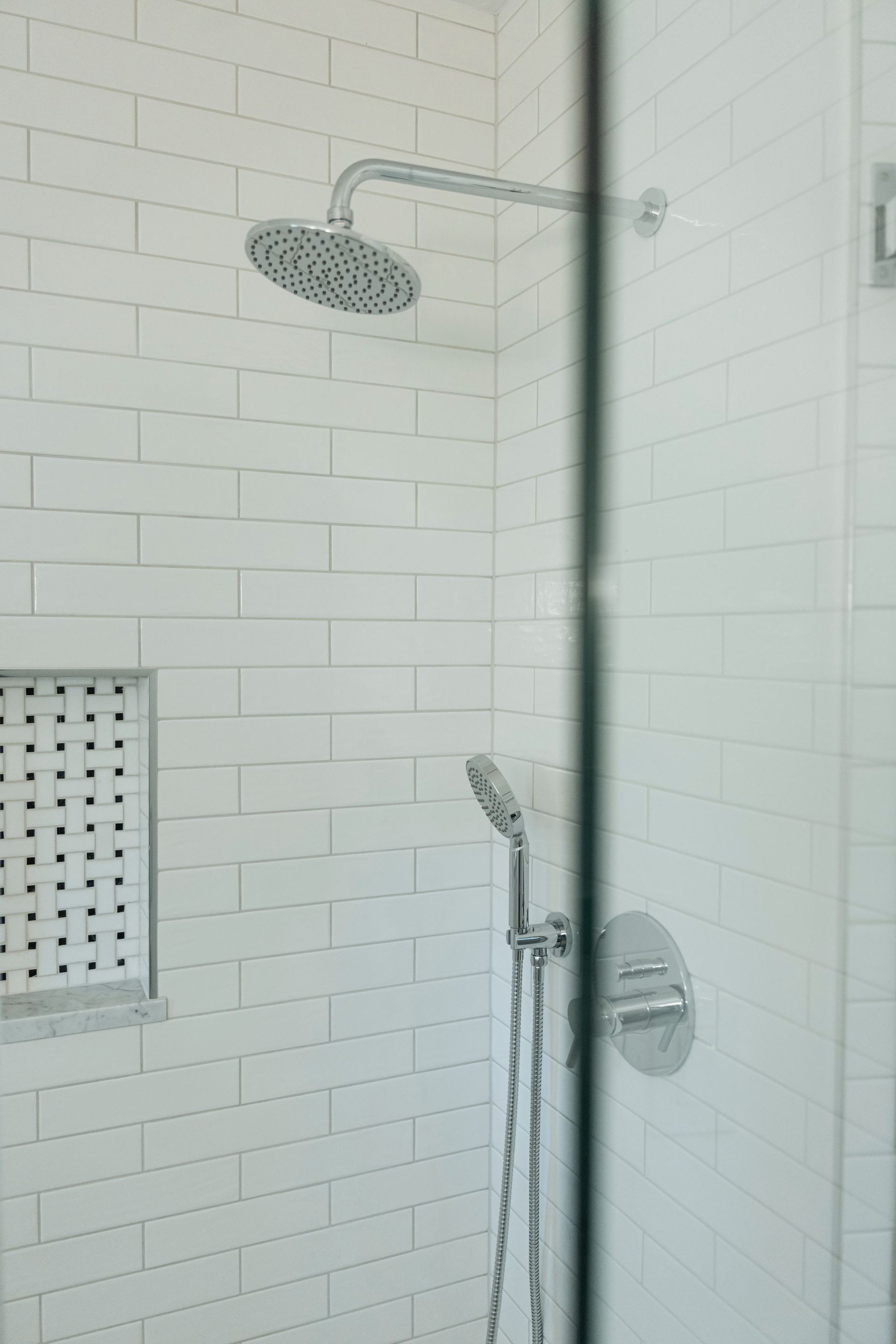 Glass shower enclosure with white subway tile, rainfall showerhead, and chrome hand shower in a bathroom