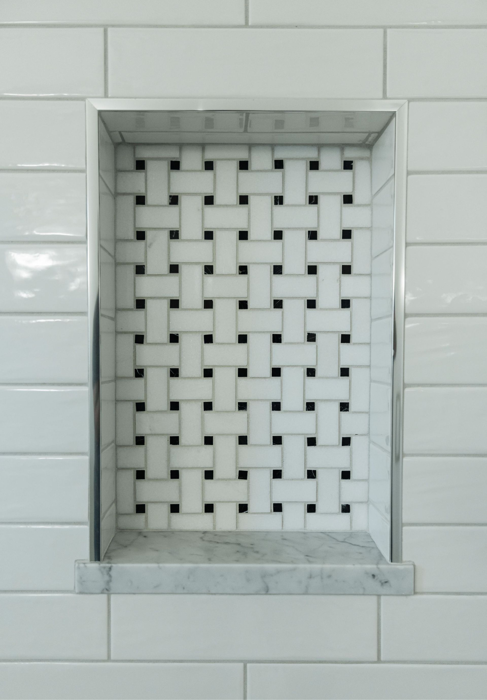 White tiled wall with a recessed window-like opening covered by a woven metal grille.