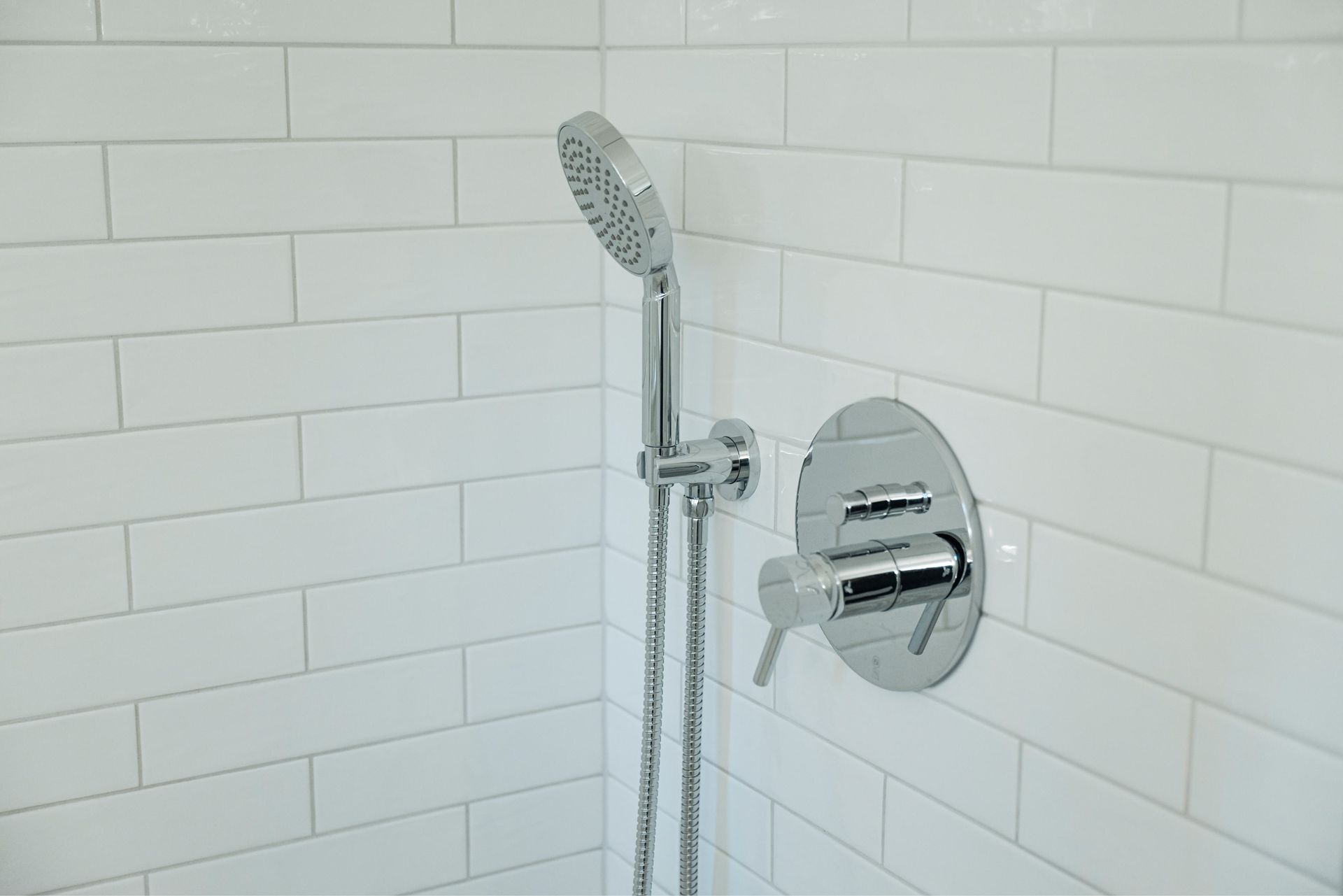 Chrome showerhead and control in a white tiled shower corner