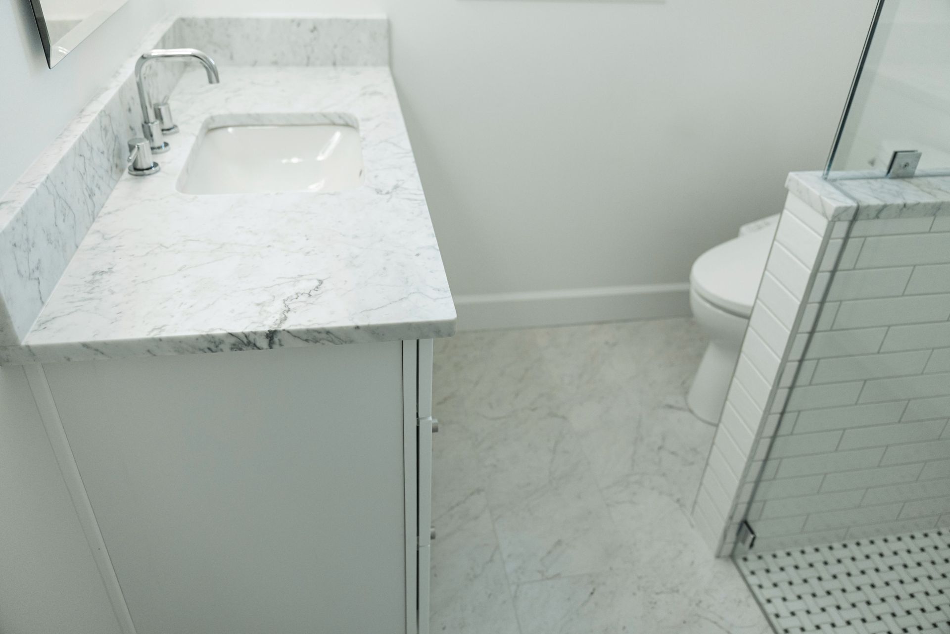 Modern bathroom with white vanity, sink, tiled floor, and toilet partly visible at right