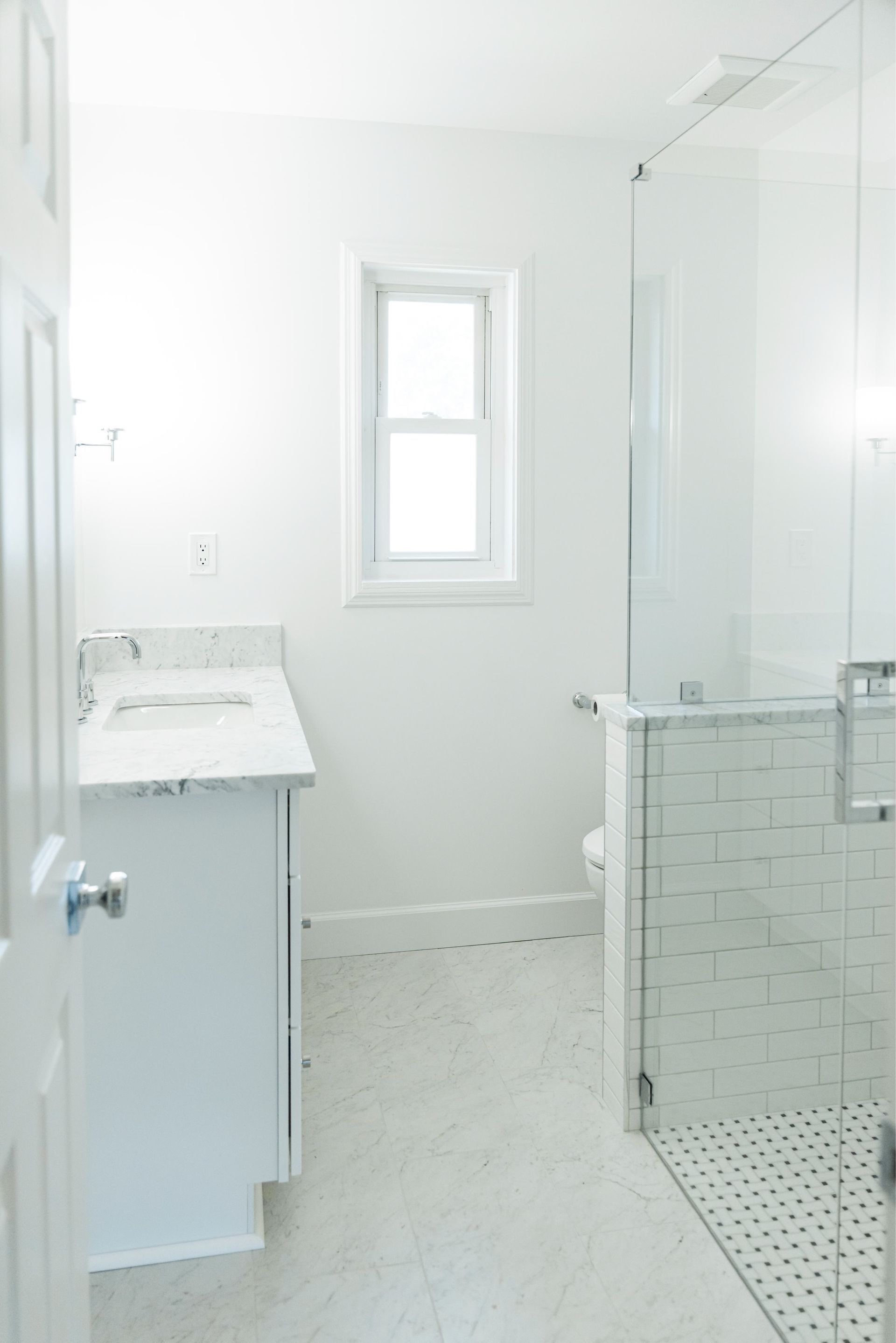 Bright white bathroom with sink cabinet, window, glass shower, and tiled floor