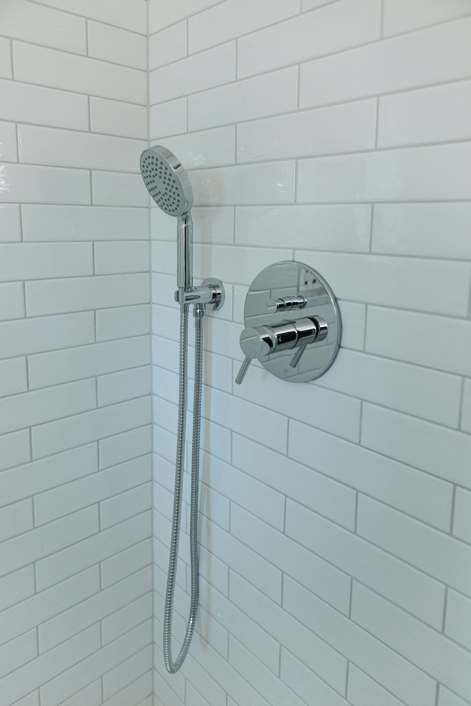 Chrome shower head and handheld shower in a white tiled bathroom corner