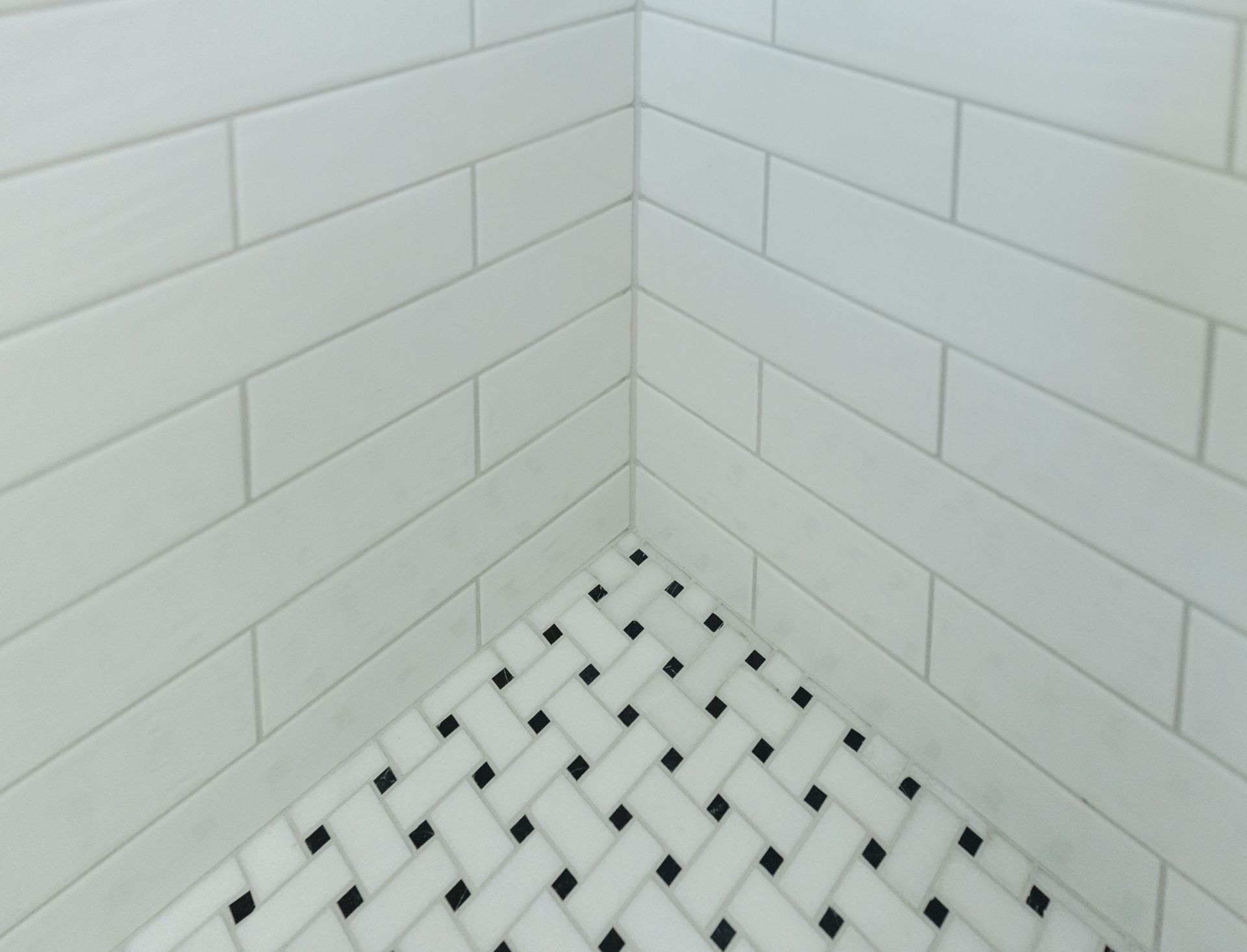 White subway tile shower corner with black-and-white mosaic floor tiles.