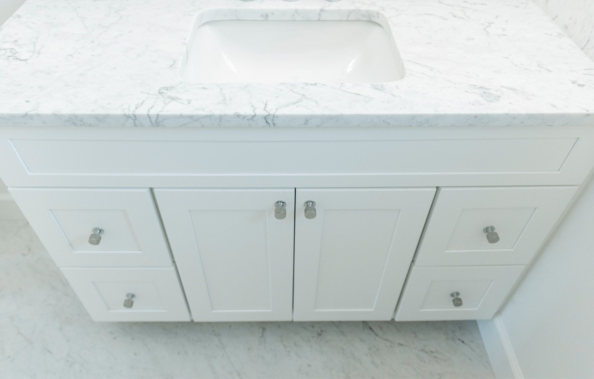 White bathroom vanity with marble countertop and built-in sink, centered against a light wall