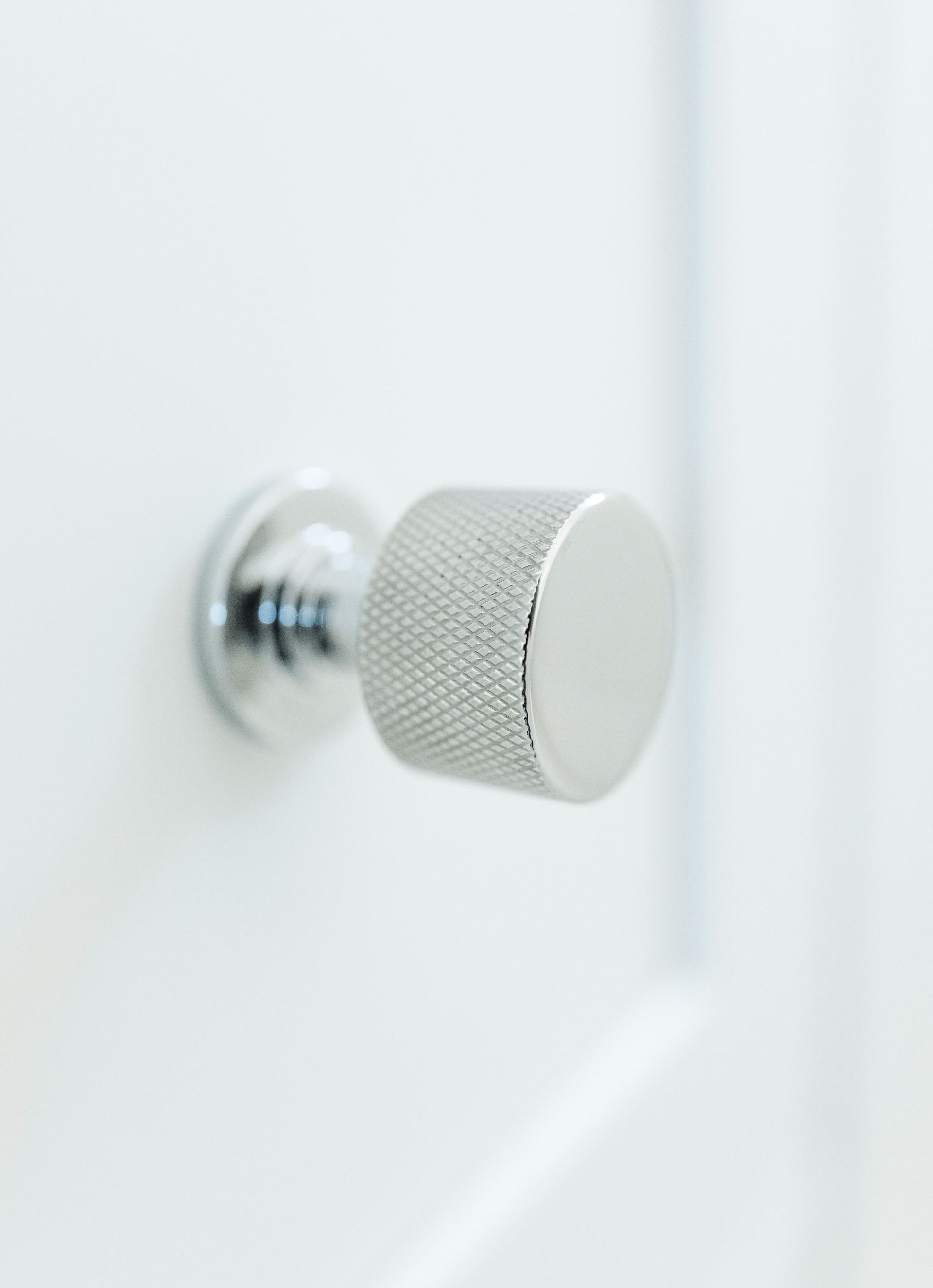 Silver textured cabinet knob on a white door panel.