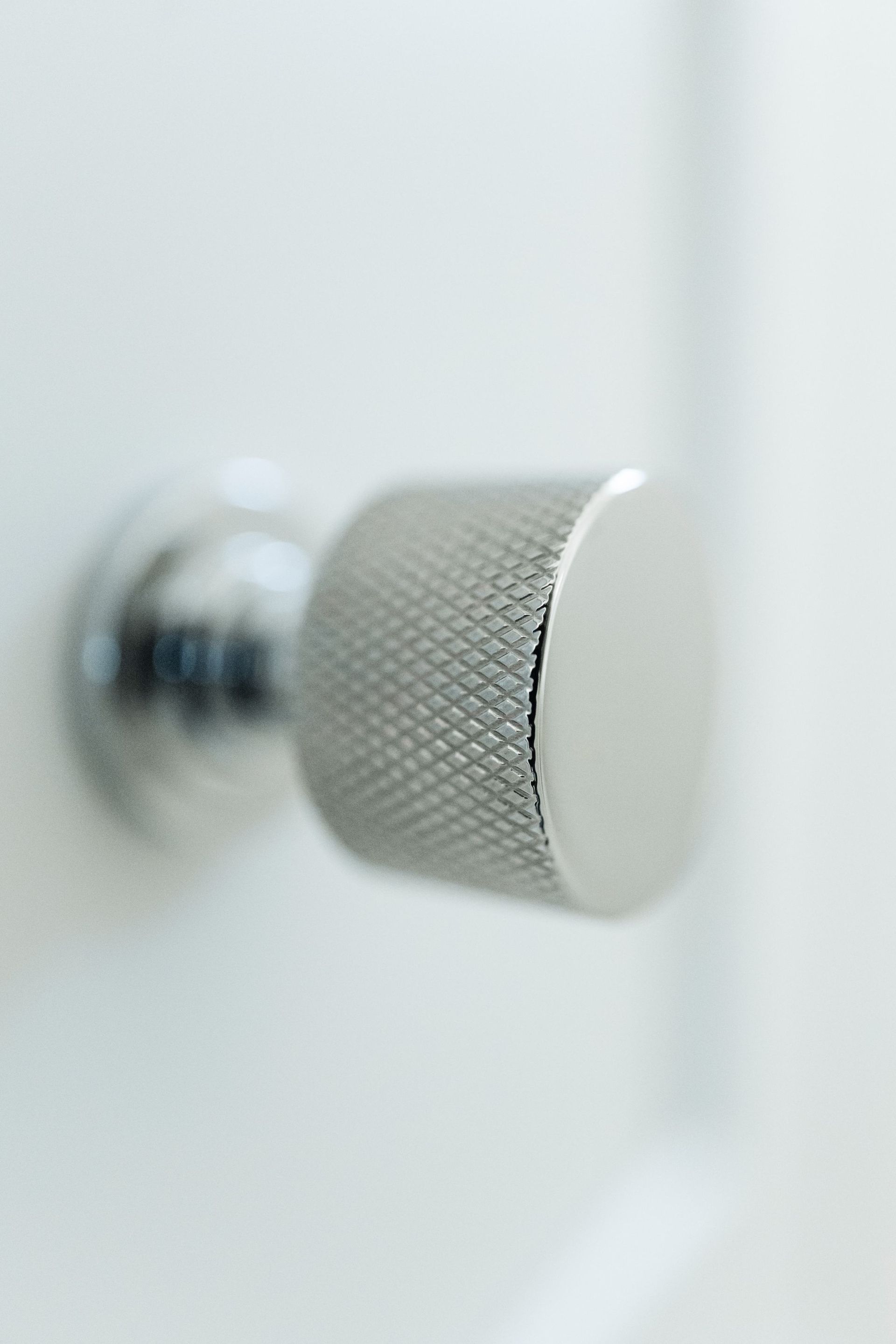 Close-up of a silver textured cabinet knob on a white door