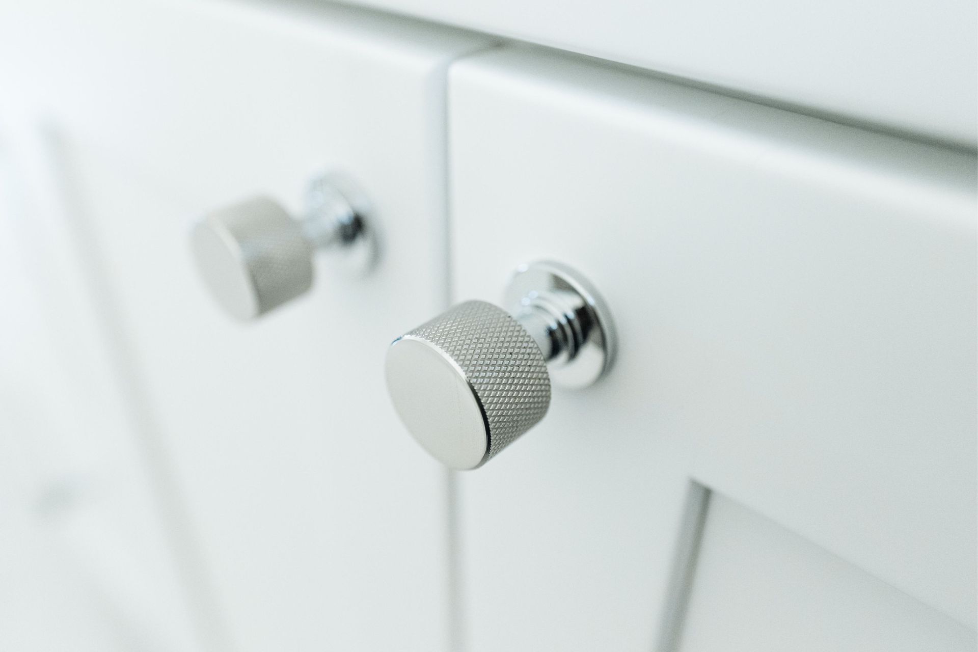 Close-up of two chrome cabinet knobs on a white bathroom vanity drawer