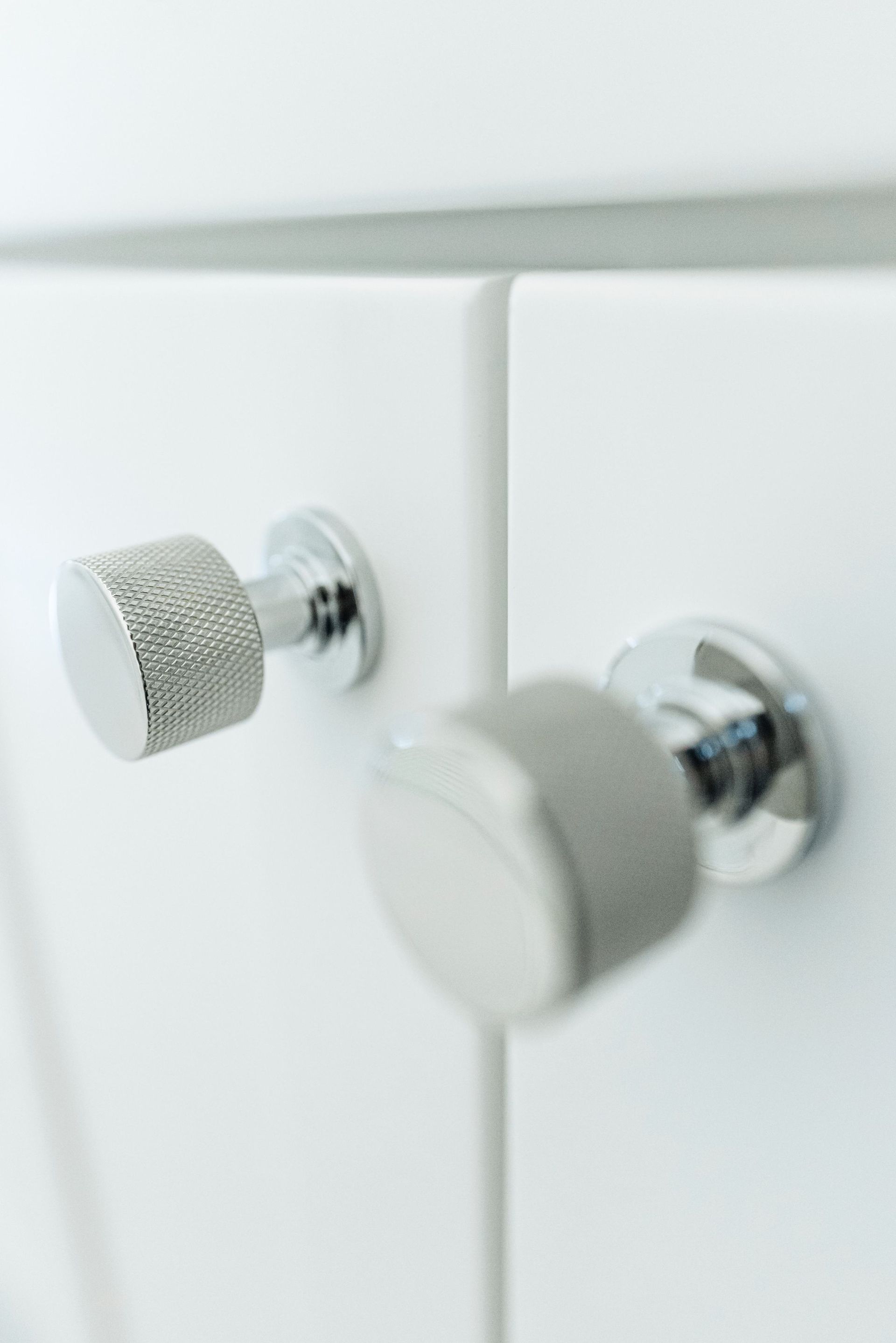 Two chrome bathroom cabinet knobs on a white cabinet door, one in sharp focus and one blurred