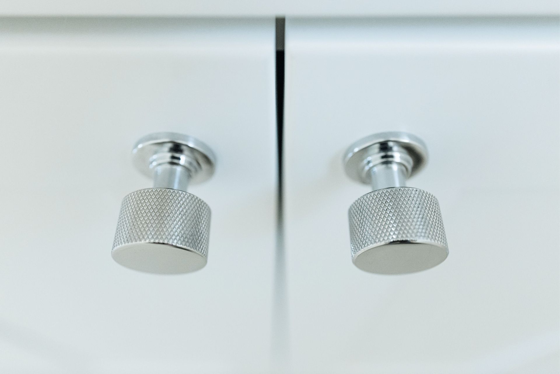 Two silver knurled cabinet knobs on white doors, viewed close up.